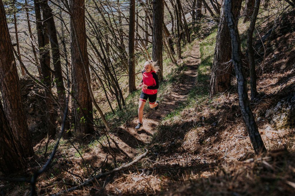 A girl on a trail running in the woods.