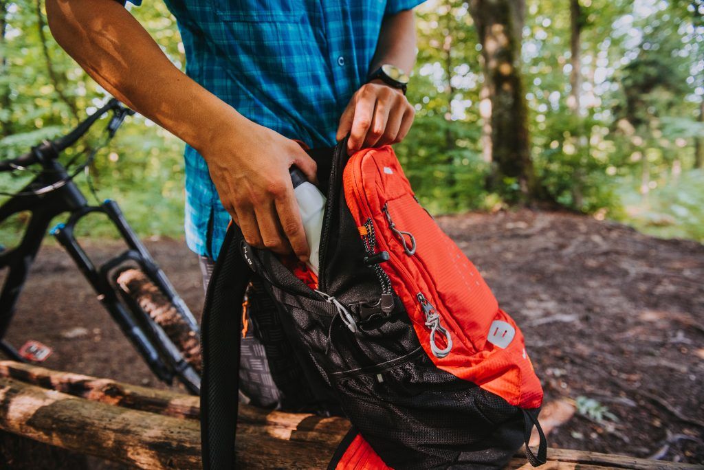 A guy putting a water bottle in his backpack.