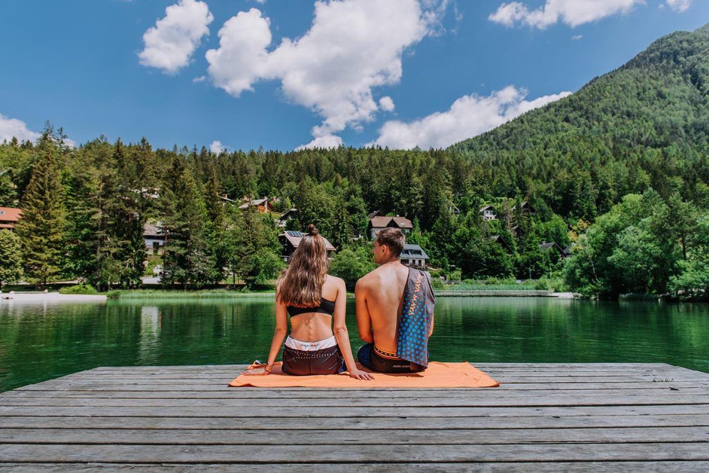 A couple sitting on a dock by a lake in the sun.