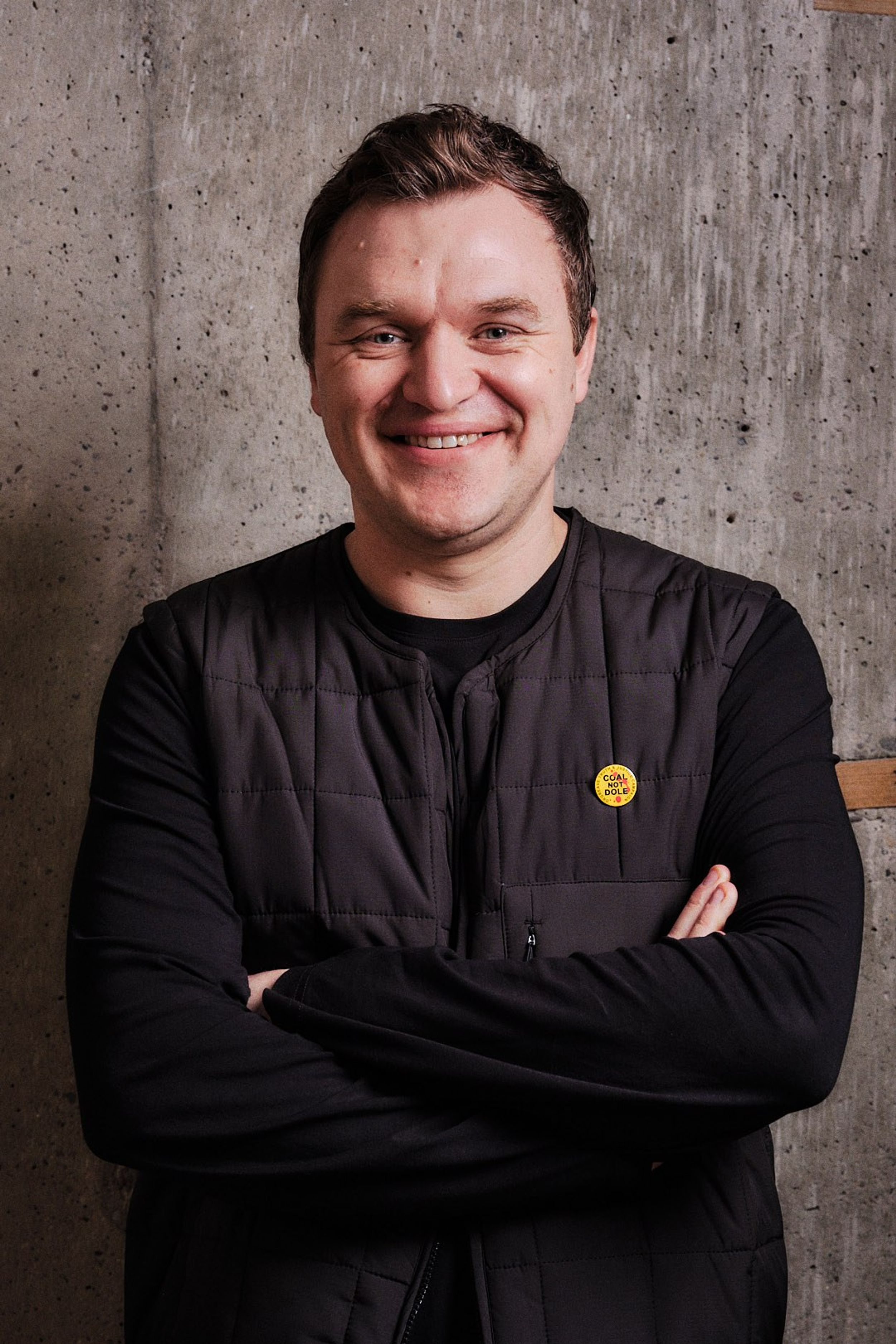 A profile shot of a man smiling with brown hair wearing a black top.