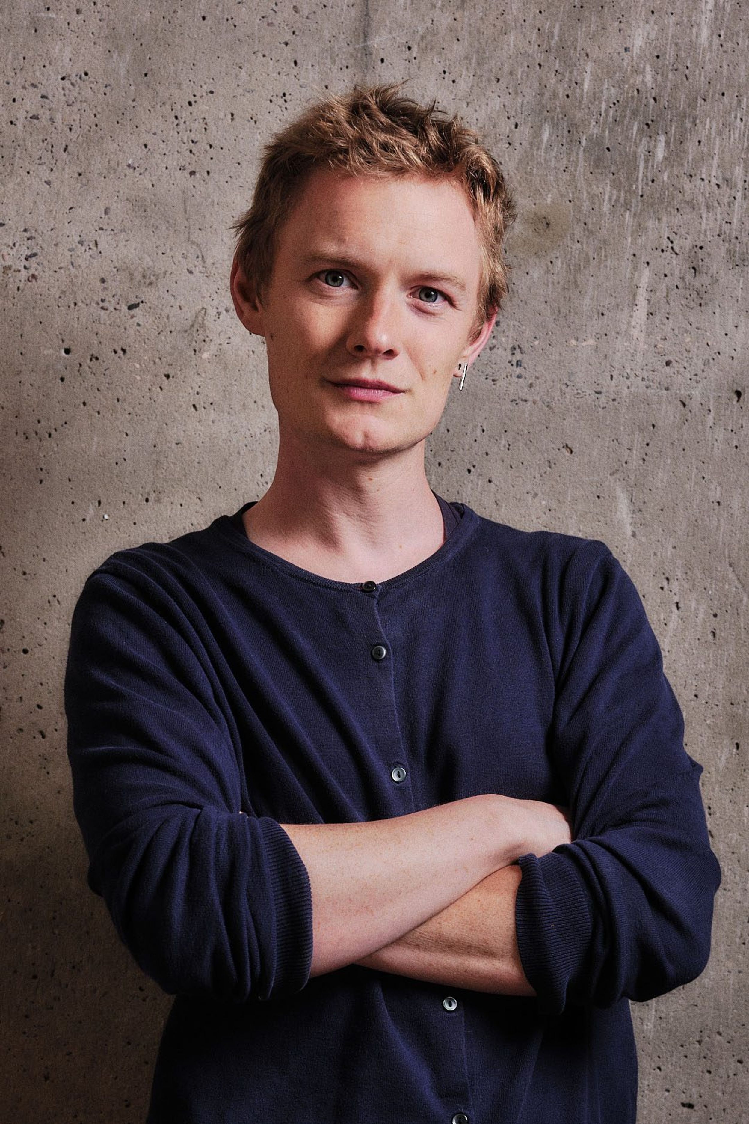 A profile shot of a person with blonde hair and crossed arms wearing a navy cardigan.