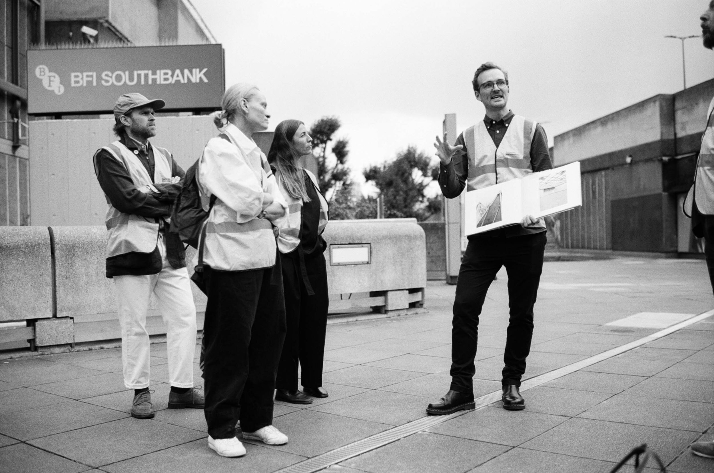 A tour guide holding a book with three people wearing hi-vis at the Southbank Centre, London.