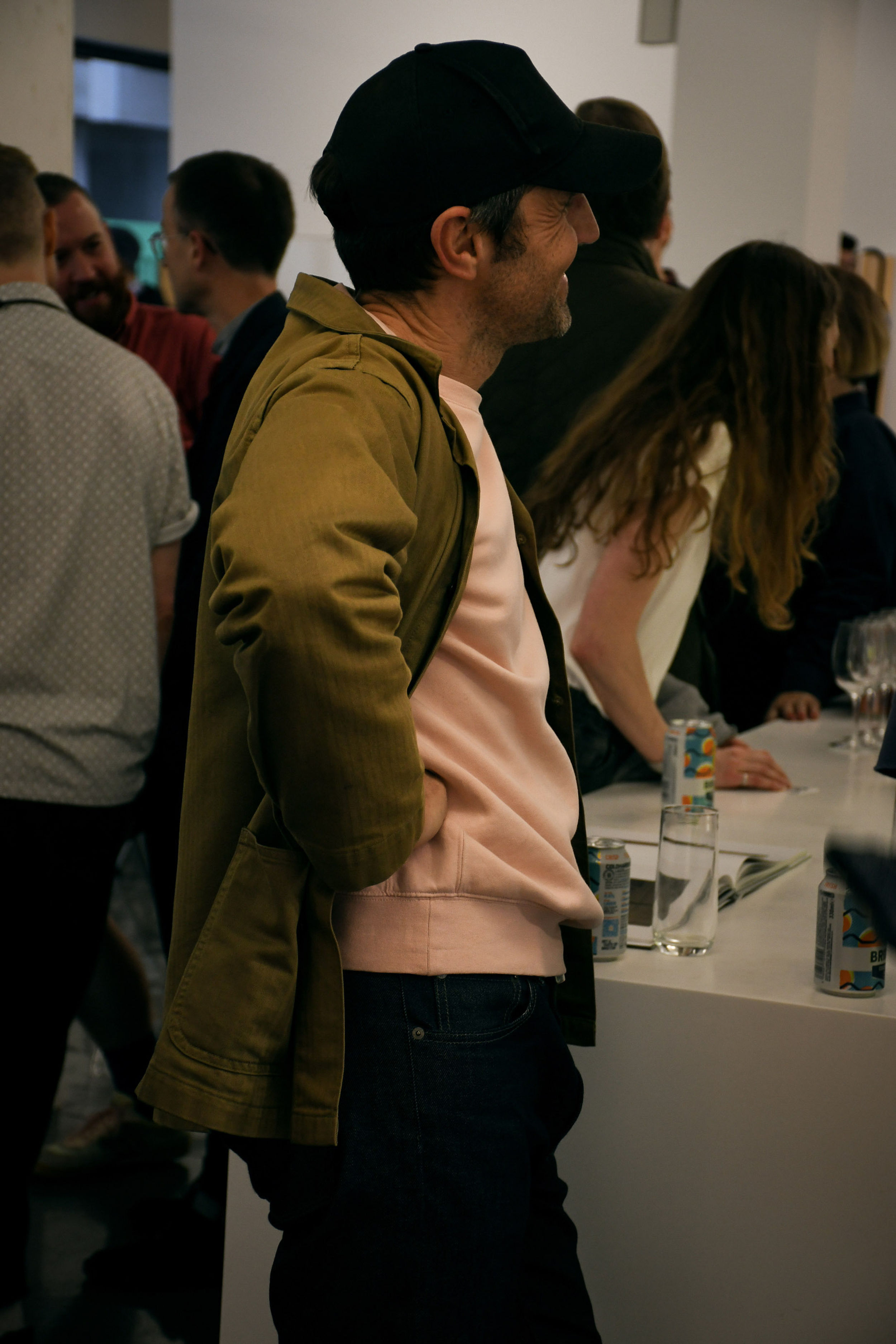 The side profile of a man wearing a pink jumper, green jacket and black cap.