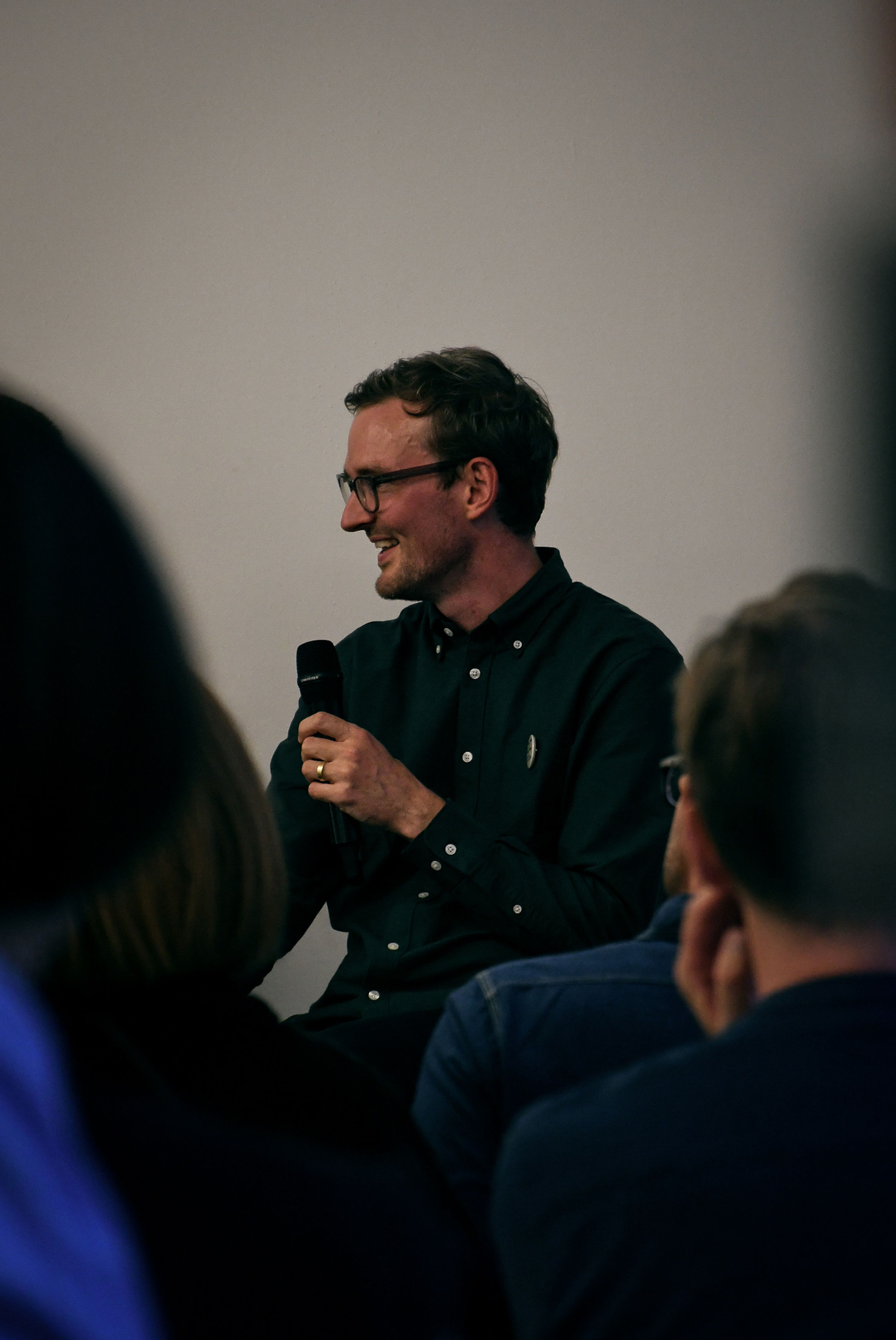 A smiling man with glasses wearing a green shirt holding a mic.