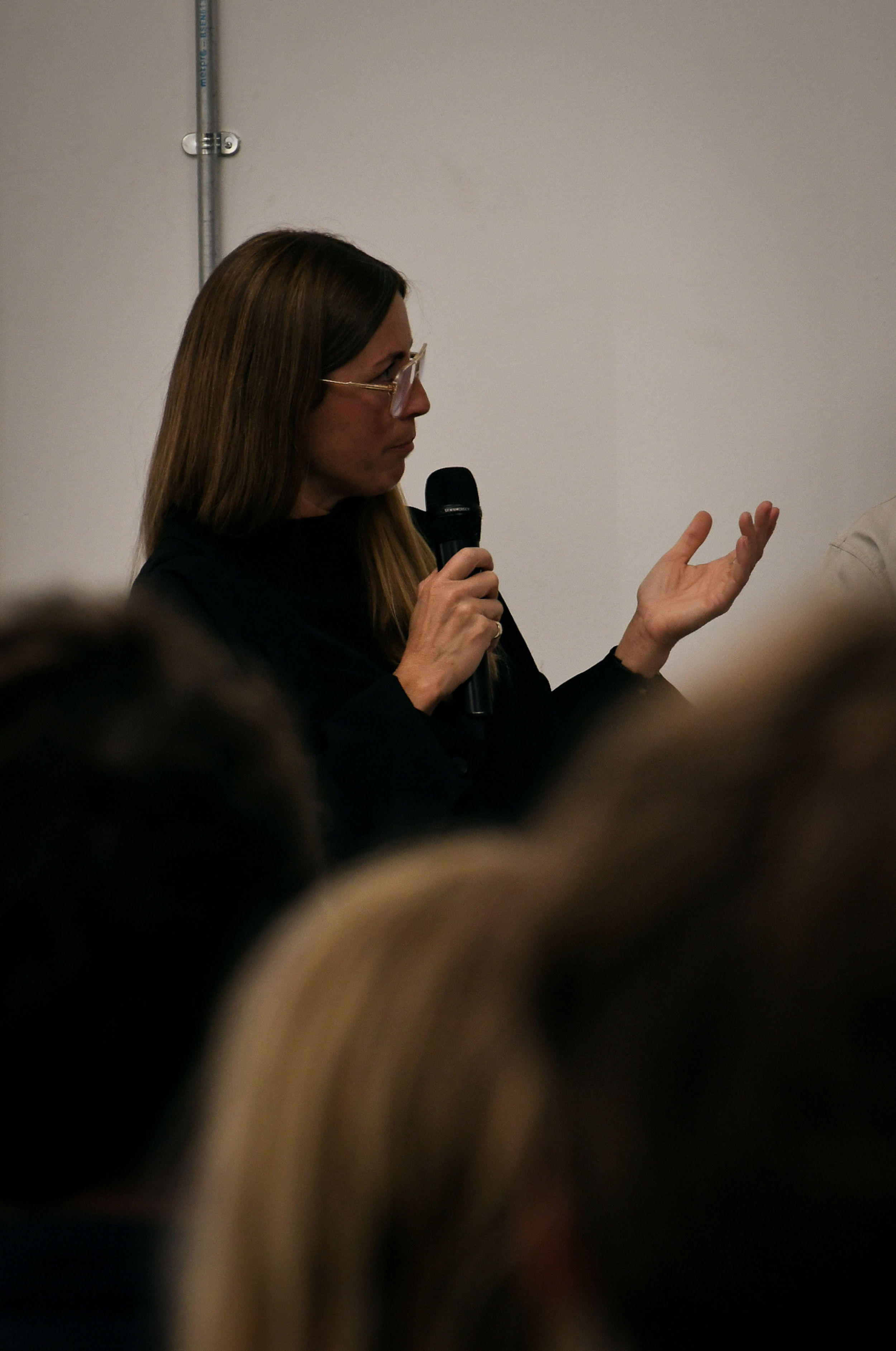 A woman with glasses holding a mic with one hand up.