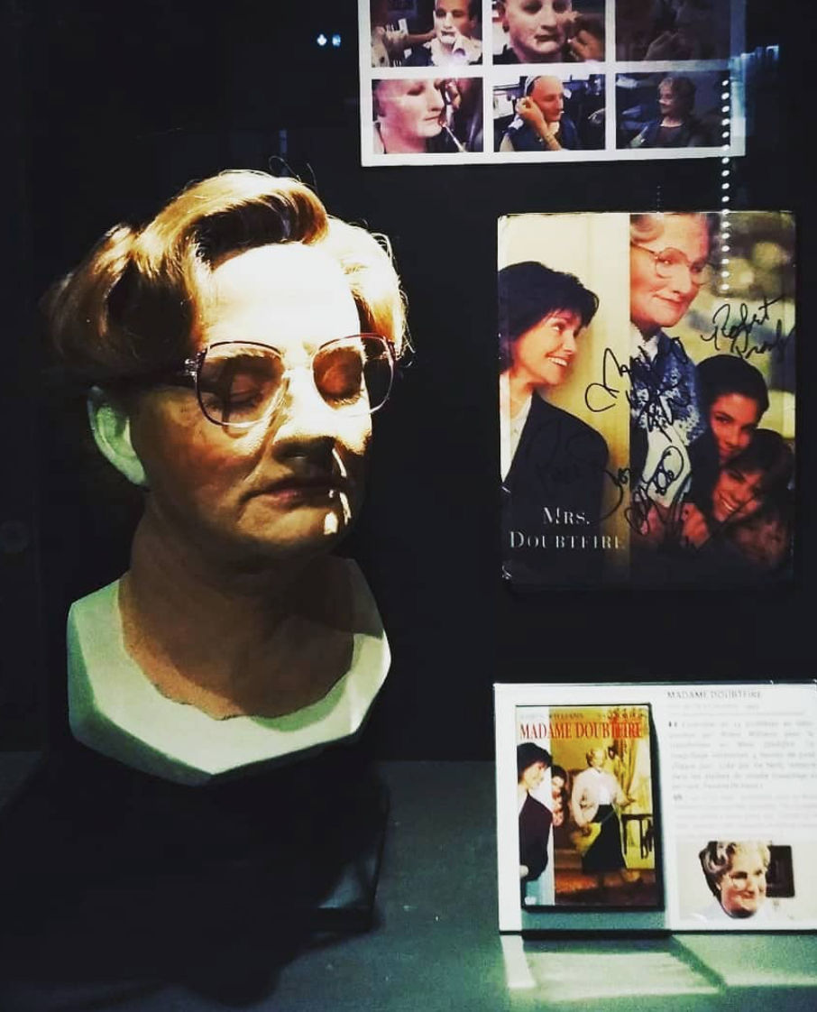 Exhibit display featuring the original prosthetic face mask used for Robin Williams’ transformation in Mrs. Doubtfire, alongside signed photos, makeup transformation shots, and promotional materials from the film.
