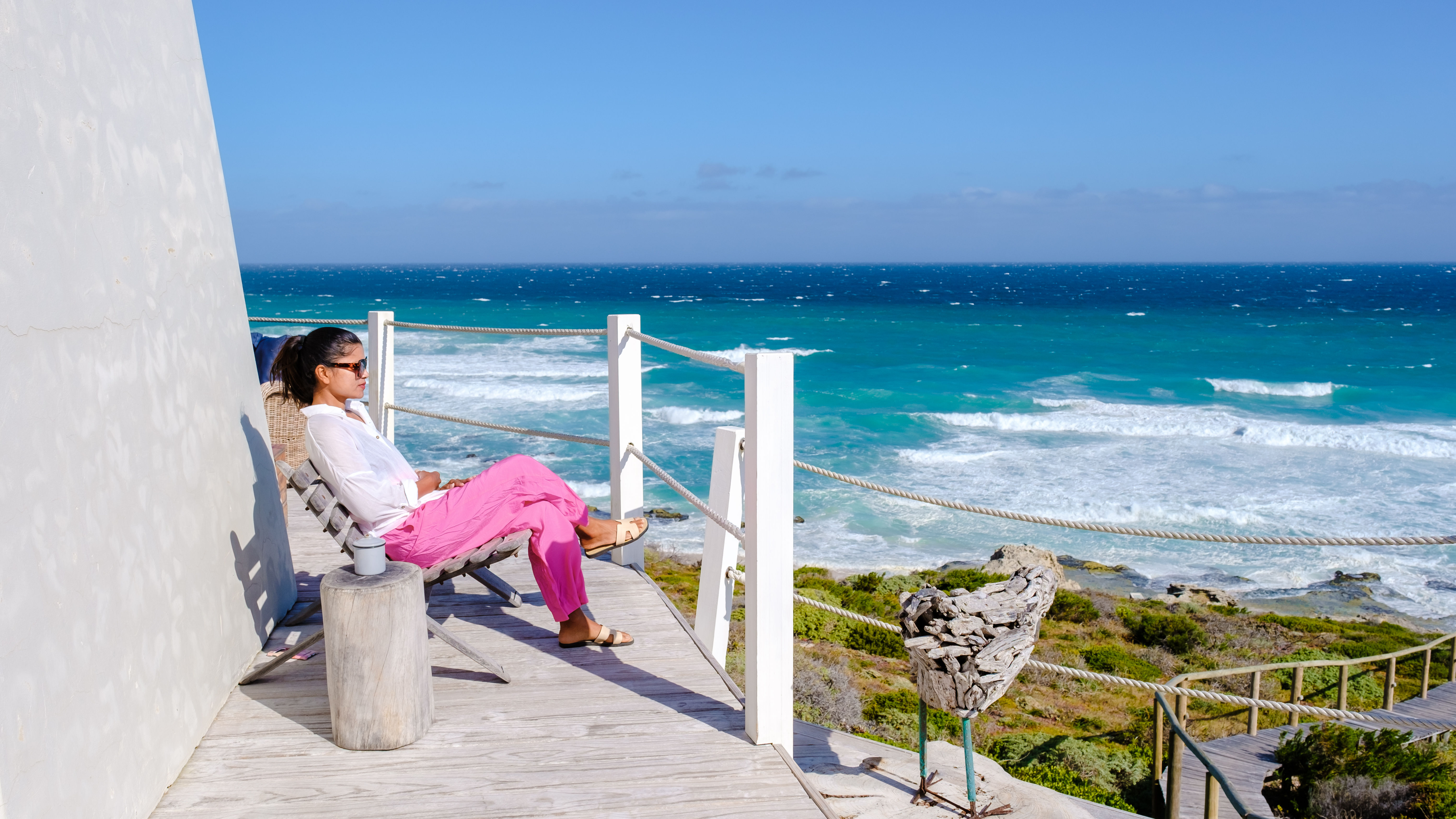 Traveler lounging on a balcony overlooking a quiet coastal village at sunset.
