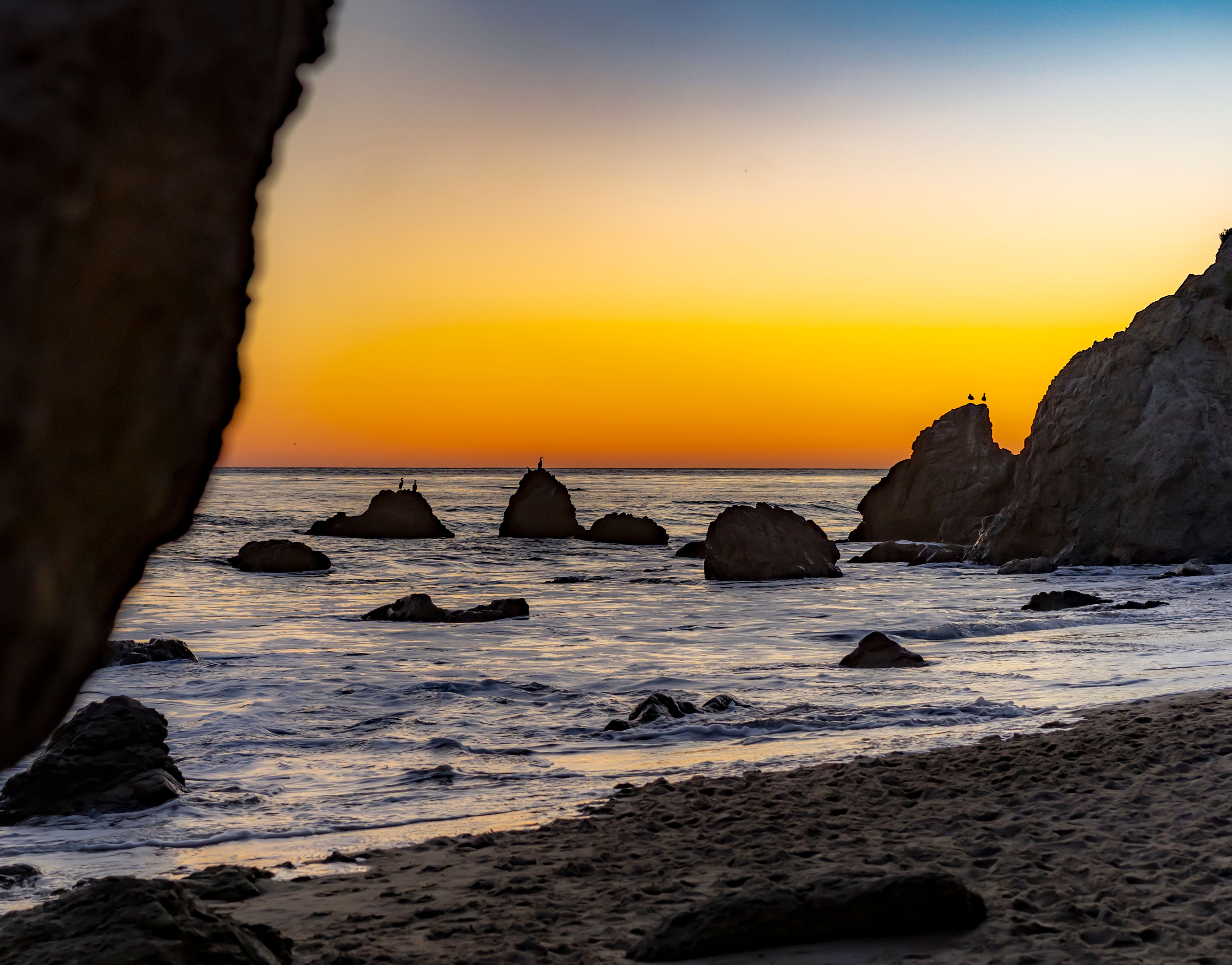 A golden California sunset behind sea stacks and arches at El Matador Beach with soft waves hitting the sand. A golden California sunset behind sea stacks and arches at El Matador Beach with soft waves hitting the sand.