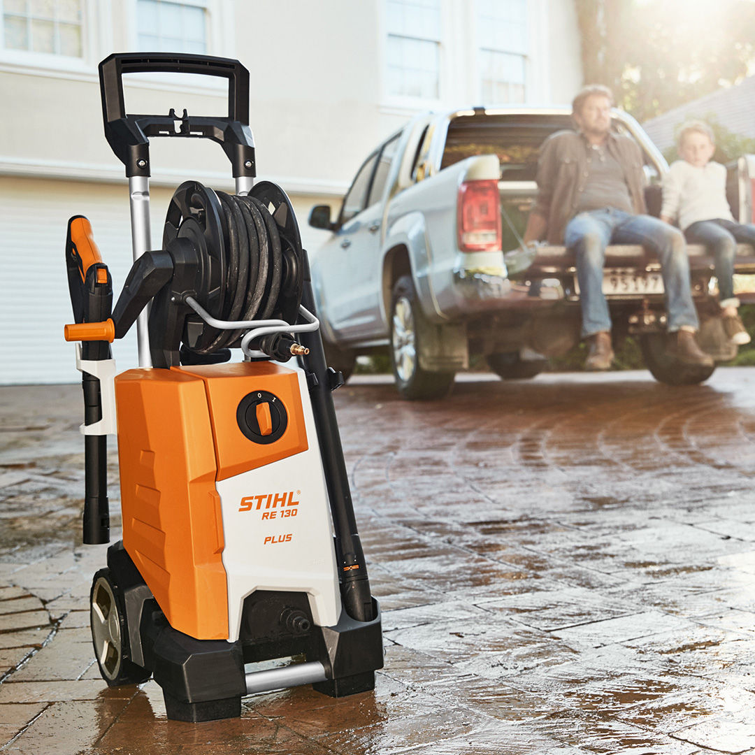 A STIHL Electric Water Blaster in the foreground with a father and a son looking satisfied sitting at the back of their car after water blasting it