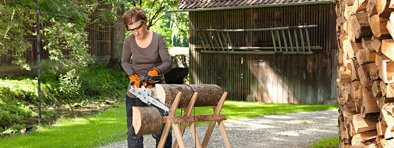 Woman cutting firewood with STIHL MSA 200 in her garden front view