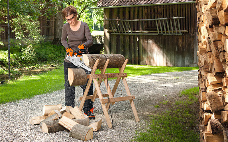 Woman cutting firewood with STIHL MSA 200 in her garden front view