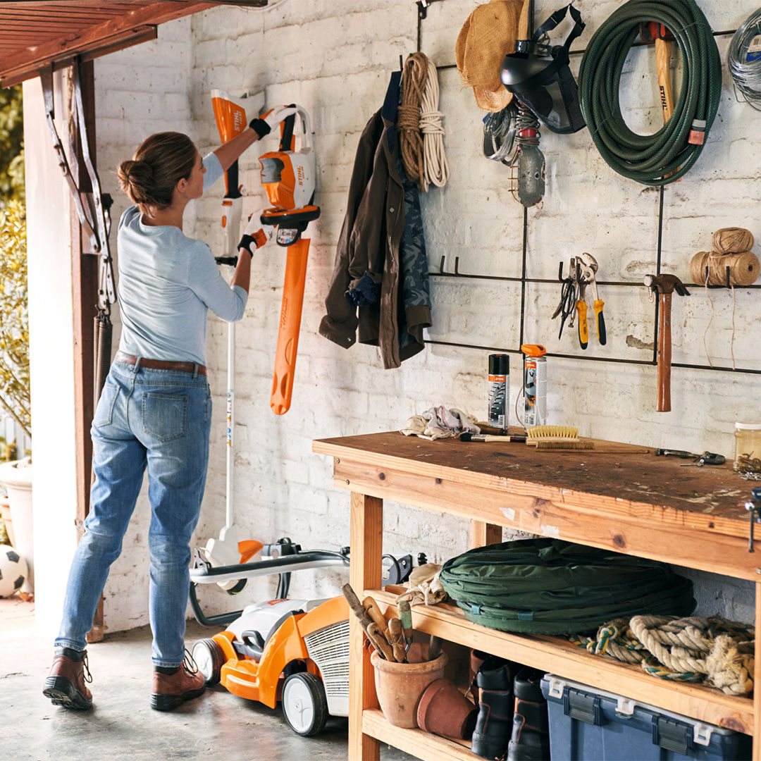 Woman hanging the cordless hedge trimmer STIHL HSA 56 on the wall.