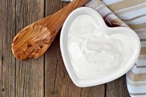 Greek yogurt in a heart shaped bowl, overhead scene against a rustic wood background