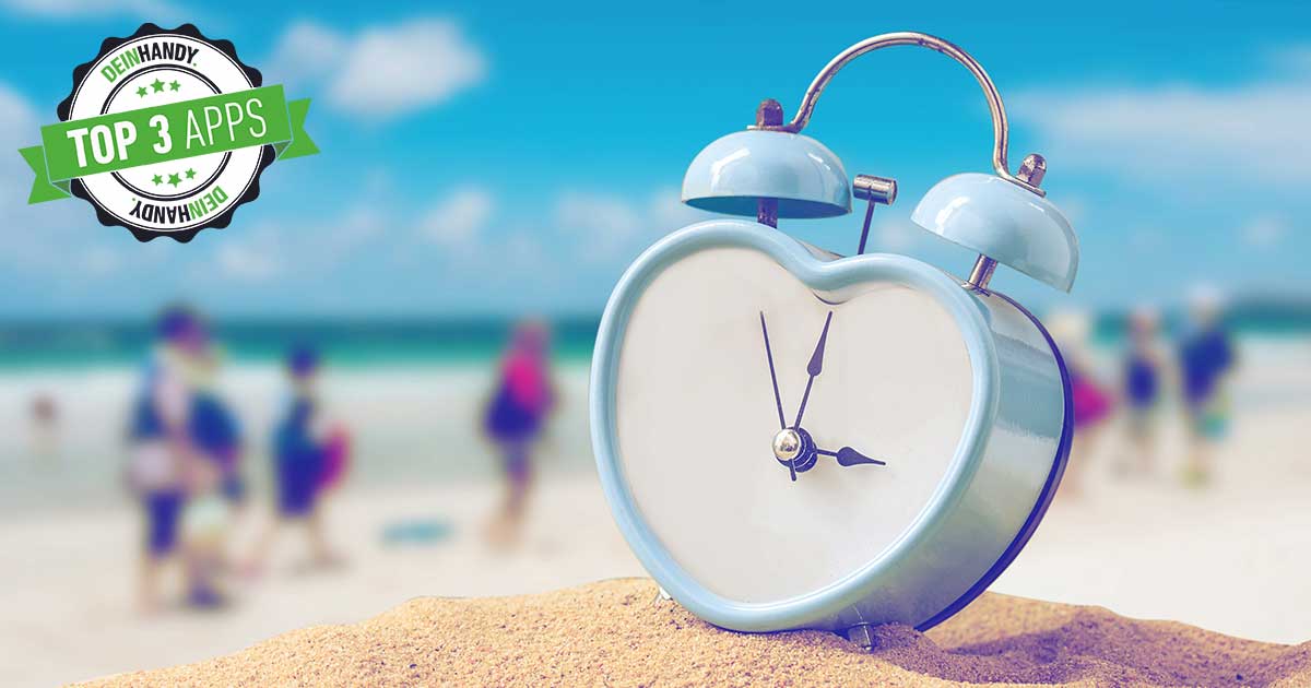 Urlaubscountdown: Herzförmige Uhr auf Sand, im Hintergrund Meer