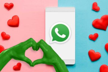 WhatsApp-Sprüche zum Valentinstag: Handy mit WhatsApp Logo, Rosa-Blauer Hintergrund. Hände, die ein Herz formen