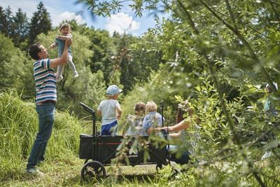 Der faltbare Bollerwagen WagonPro mit einem praktischen Dach und Platz für 4 Kinder macht jeden Ausflug zu einem Abenteuer mit Entspannung für Eltern und Kind. Hier sieht man eine Familie, welche einen warmen Sommertag im Wald verbringt und dabei den Platz vom Bollerwagen für Kind und Gepäck nutzt.