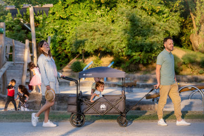 Der faltbare Bollerwagen SmartCruiser City mit einem praktischen Dach und ganz viel Platz macht jeden Ausflug zu einem Abenteuer mit Entspannung für Eltern und Kind. Hier sieht man eine Familie, welche einen warmen Sommertag nutzt um mit dem Bollerwagen den Park zu erkunden.