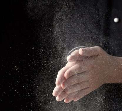 Chef hands in flour on black background banner. Making pizza, pasta, baking bread and sweets. Clap with splash of white flour with copy space.