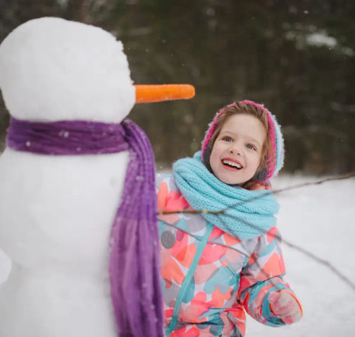 A happy child making a snowman outside of a ski resort