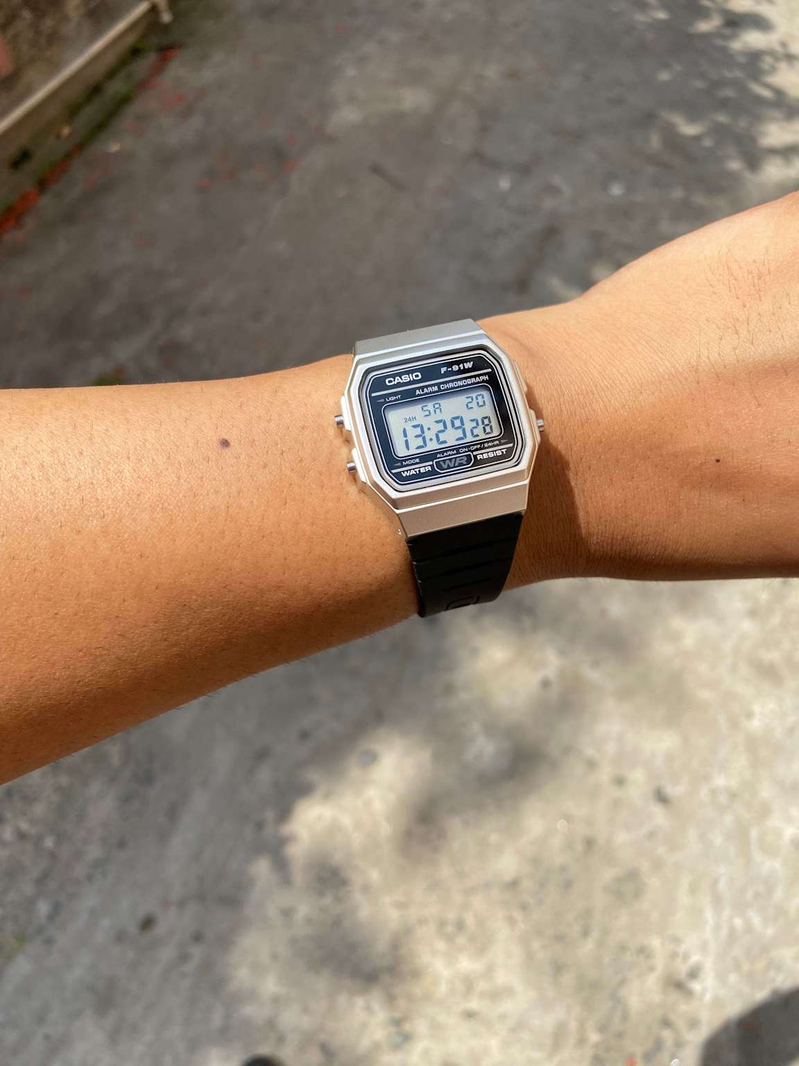 Casio F-91W digital watch on wrist showing time and date in a natural outdoor setting