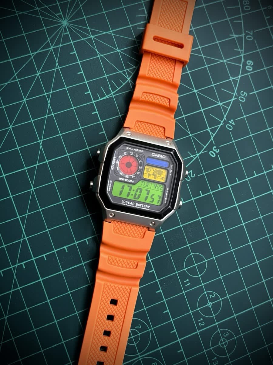 Custom Casio AE-1200 watch with an orange strap and modified dial design, shown on a crafting mat to illustrate watch modding