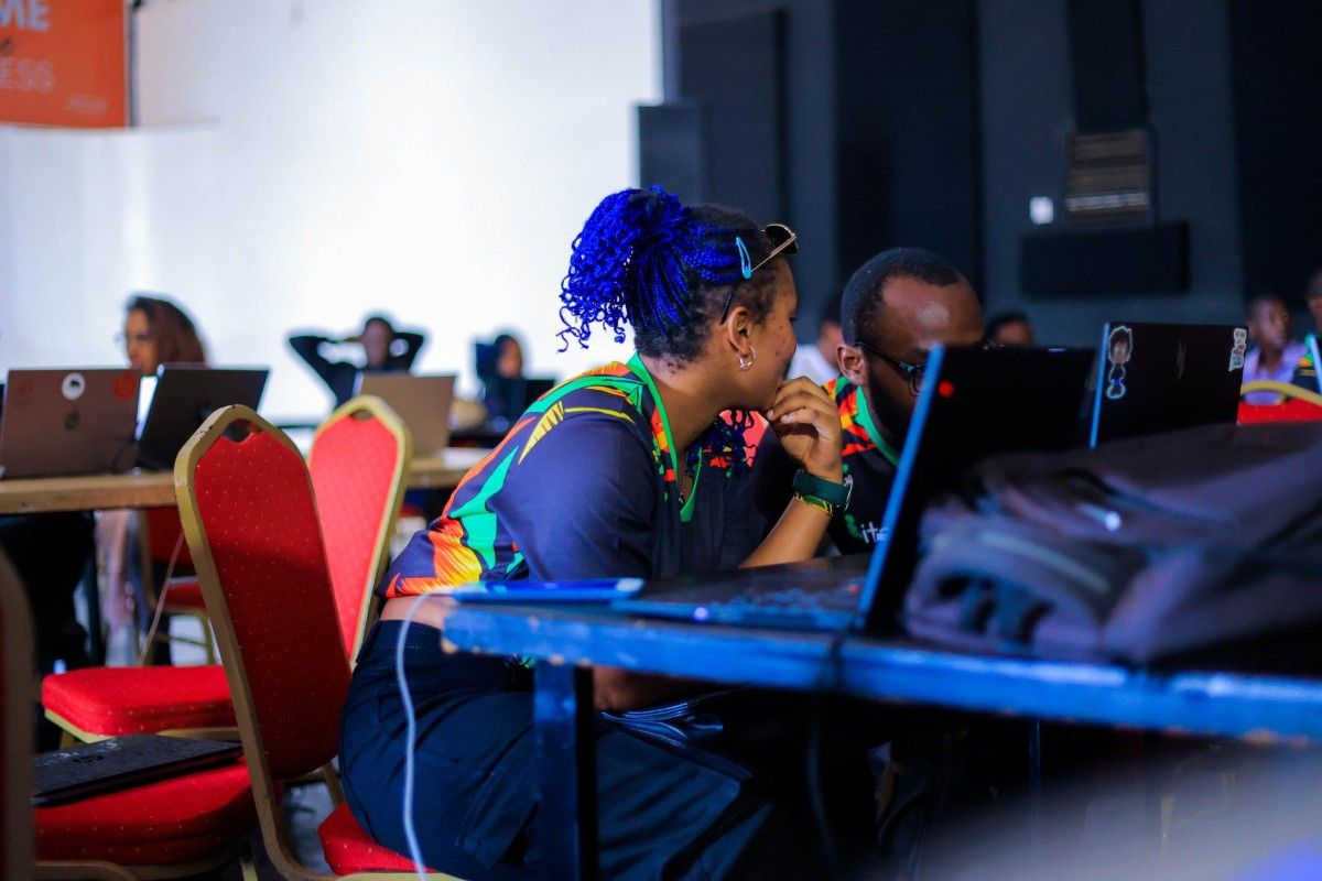 A female attendee at the Bitnob Developer Event in Kampala 2025 Whispering to a male attendee sitting next to her