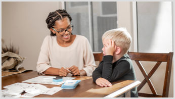 A female teacher smiling while explaining a topic to a young boy.