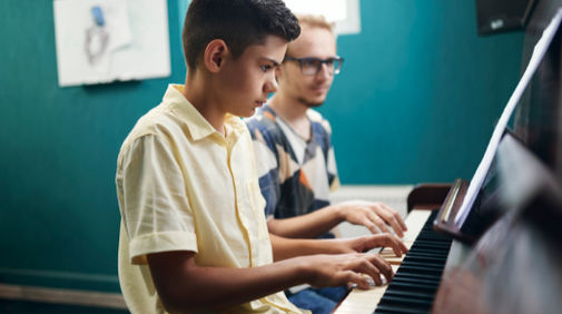 A student playing the Piano with his teacher sitting alongside. A student playing the Piano with his teacher sitting alongside.