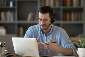 A tutor explaining a topic in front of his laptop for a virtual lesson.