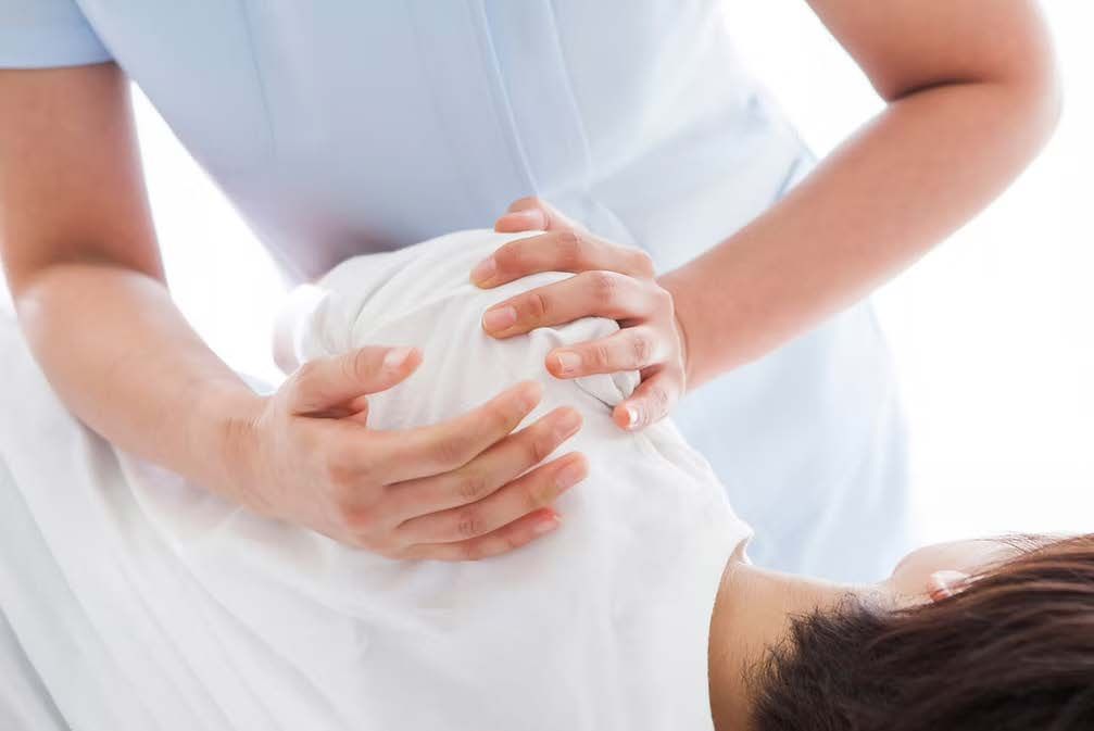 a person laying on their right side, receiving an adjustment of their left shoulder from a chiropractor