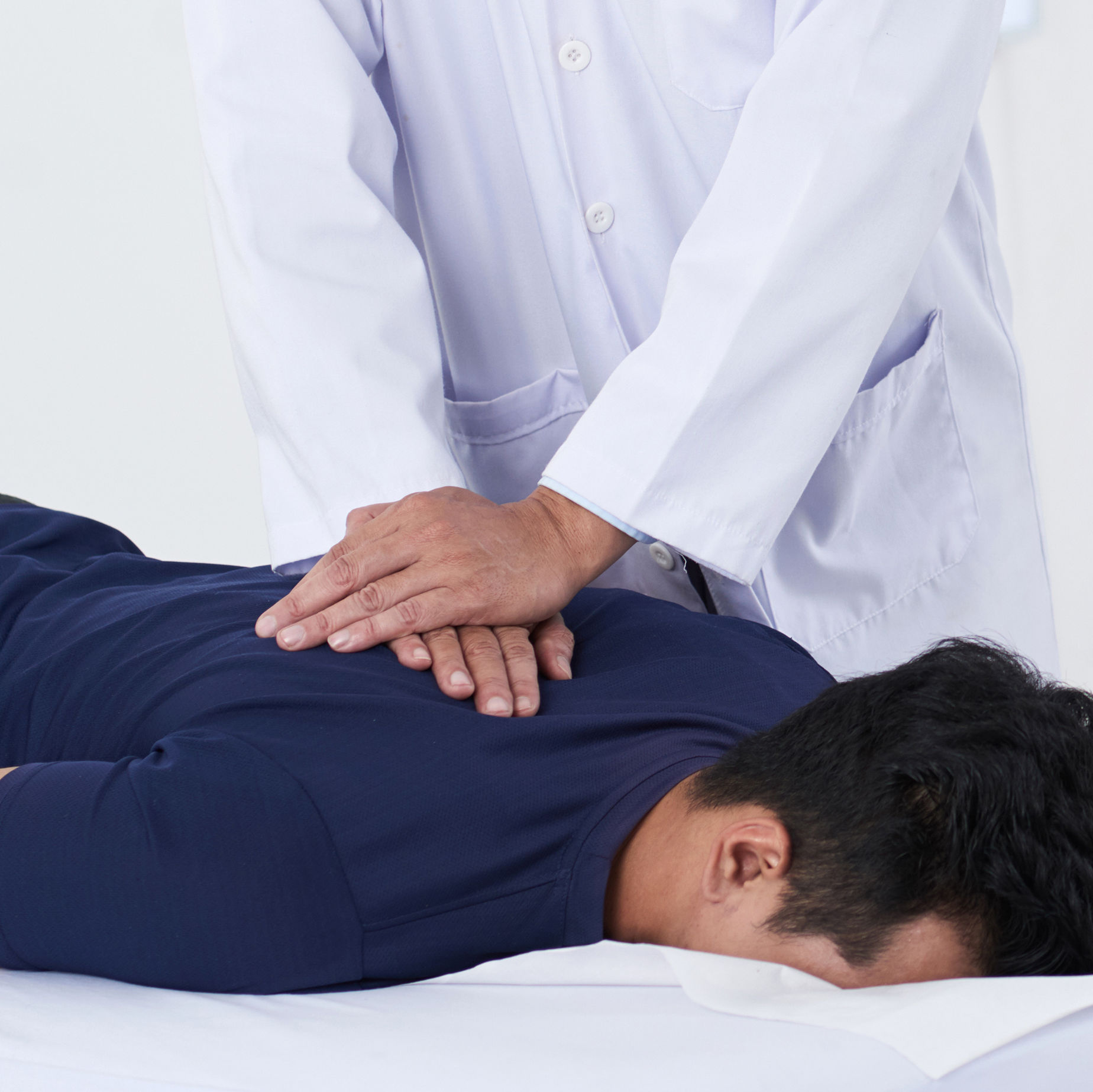 A healthcare professional performs a spinal adjustment on a patient lying face down on a treatment table in a clinical setting.