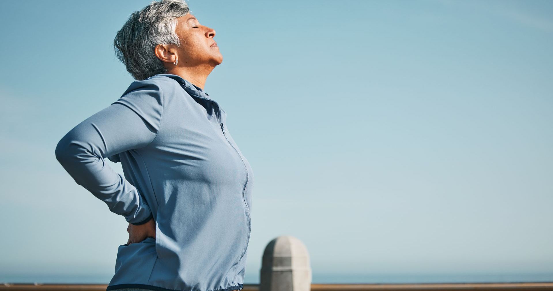 Senior woman outdoors in sportswear holding lower back in discomfort, symbolising chronic back pain needing chiropractic care.