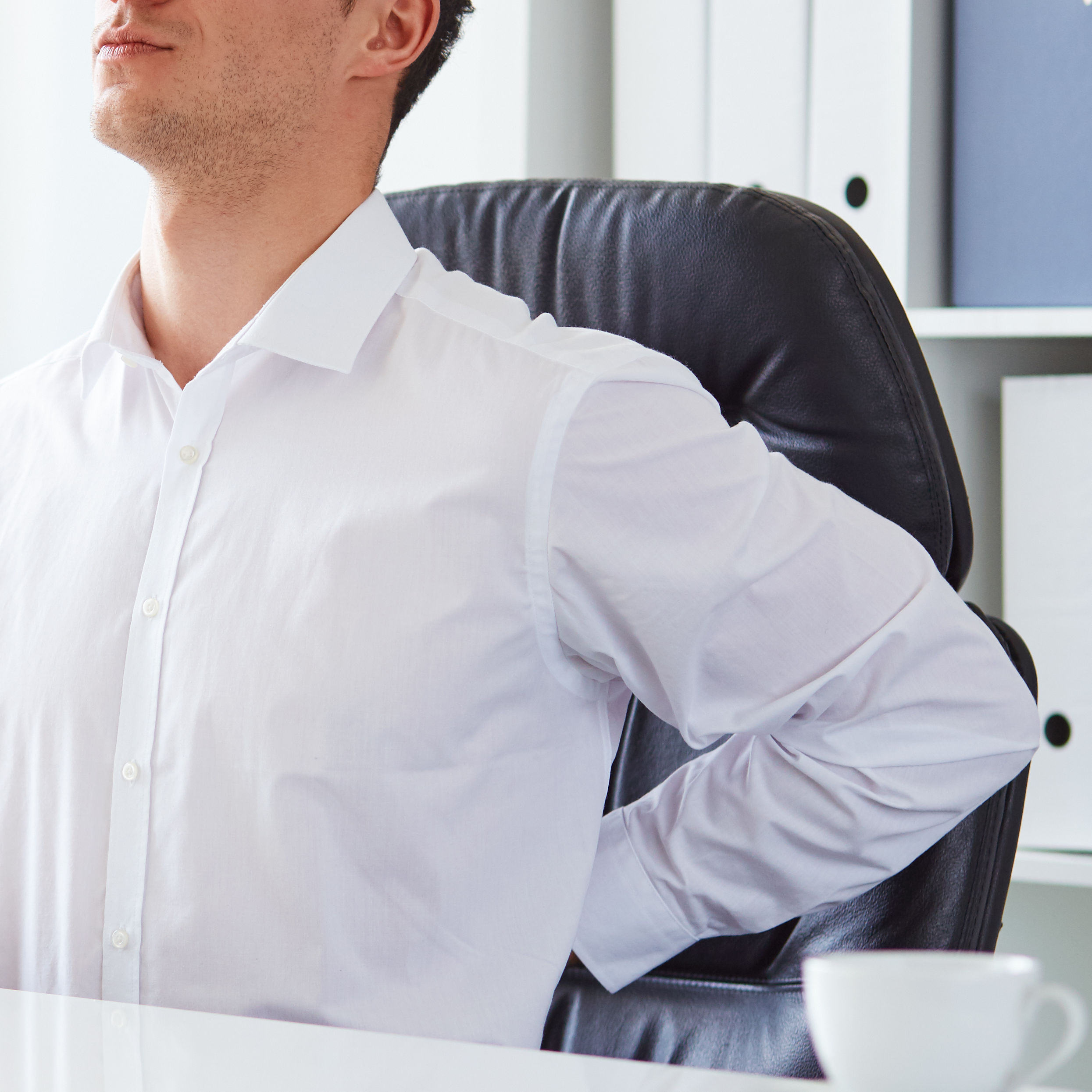 young white business man at laptop holding left arm to low back pain