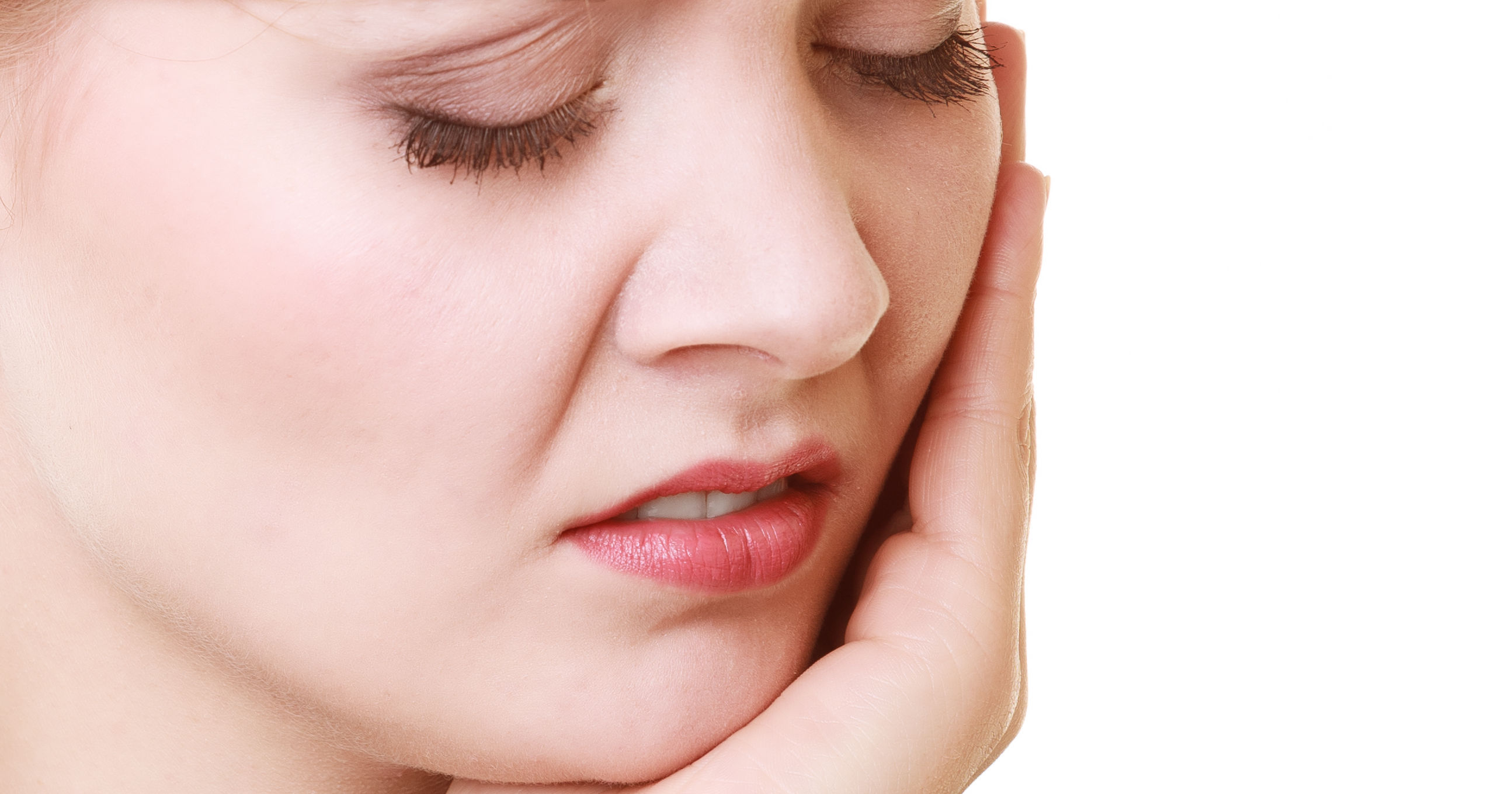 A woman holds her jaw with a pained expression, indicating discomfort or distress, against a plain background.