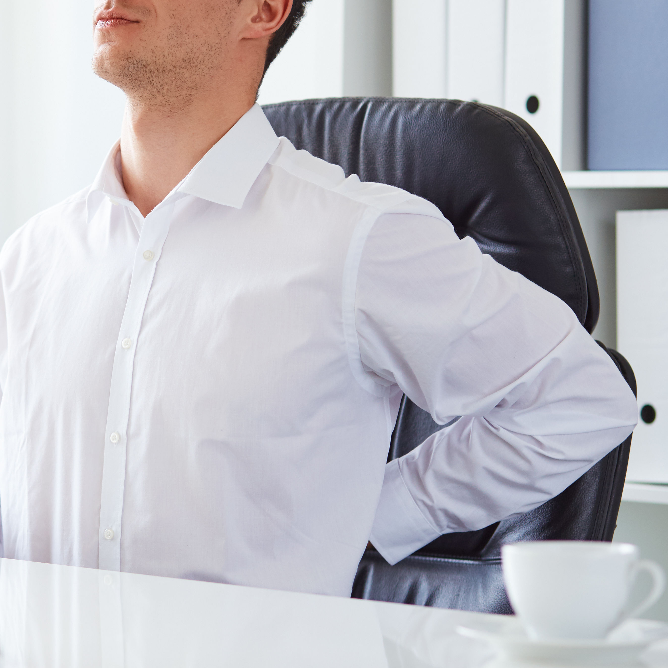 young white business man at laptop holding left arm to low back pain