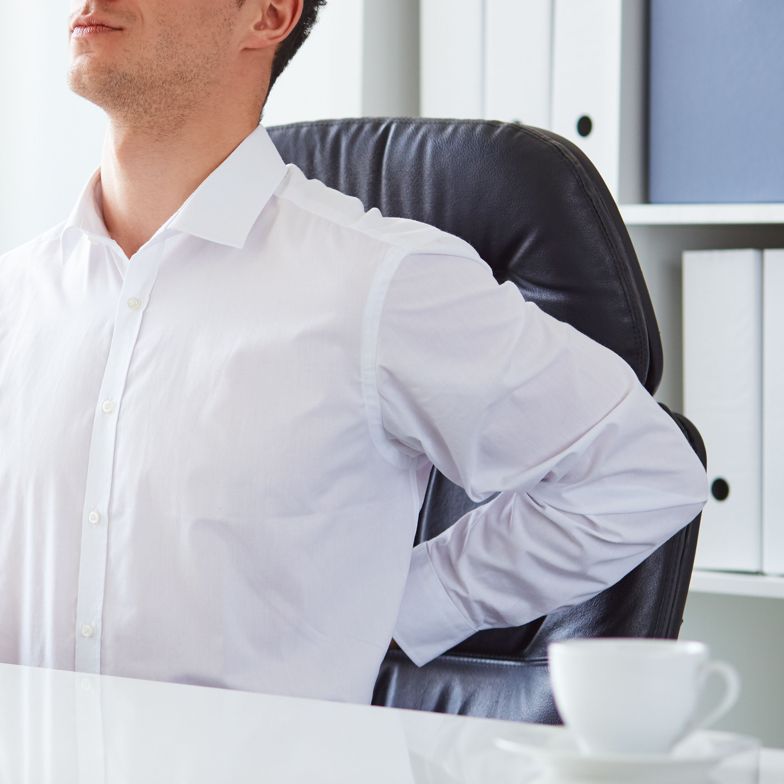 young white business man at laptop holding left arm to low back pain