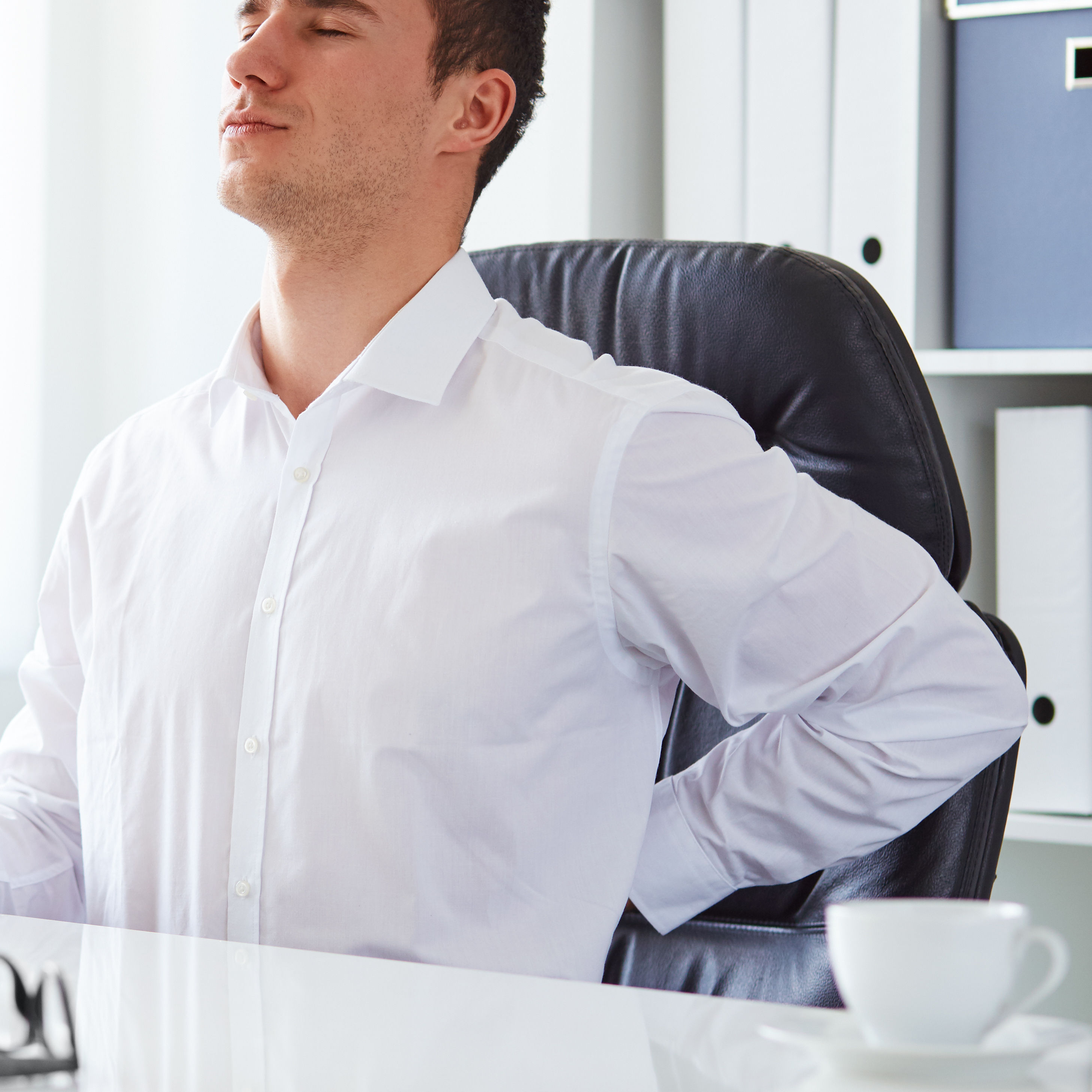 young white business man at laptop holding left arm to low back pain