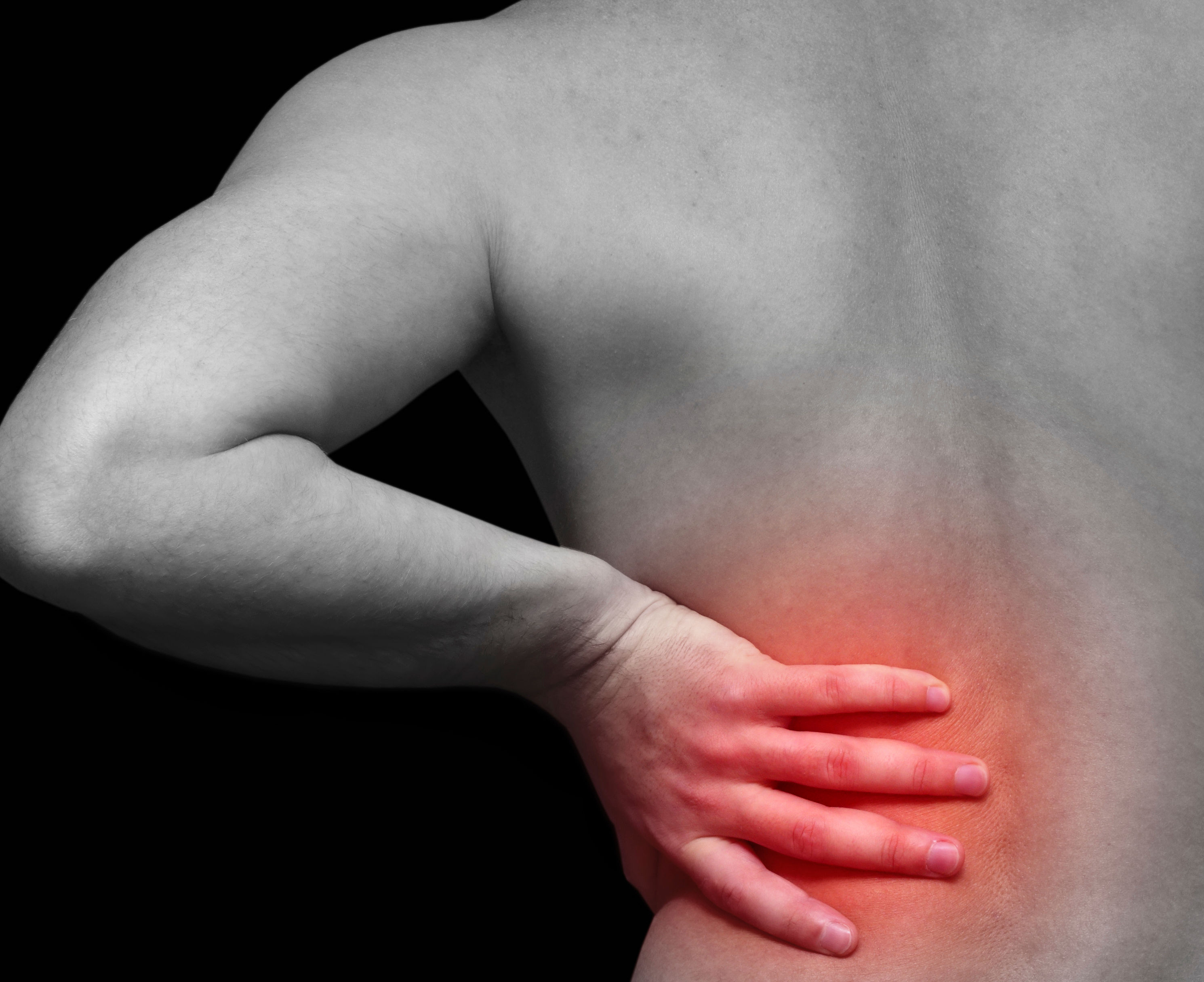 The image shows a close-up of a person’s back, highlighting a hand placed on the lower back, indicating pain or discomfort, with a dark background.