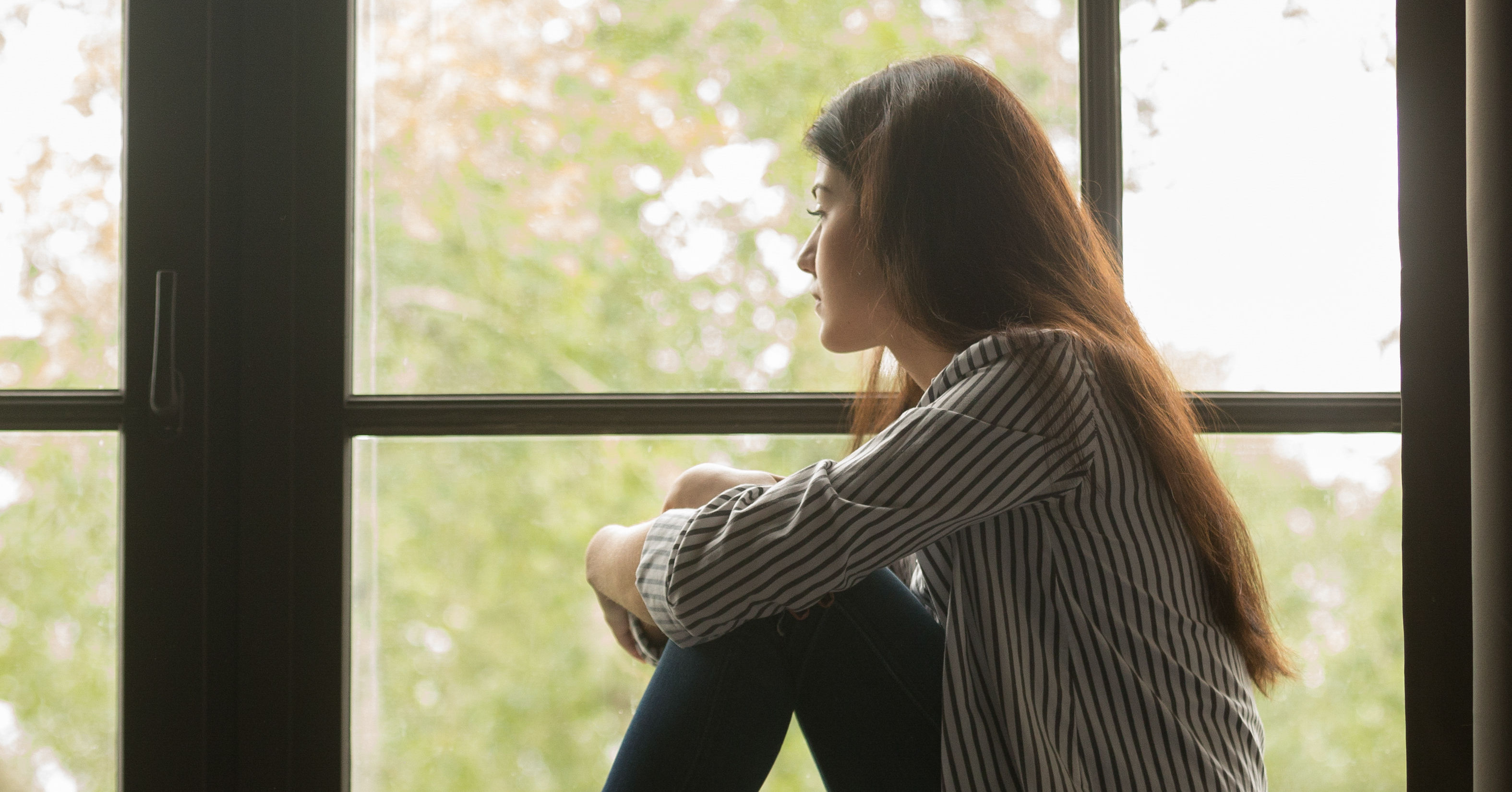 Sad young woman sitting looking out window and thi