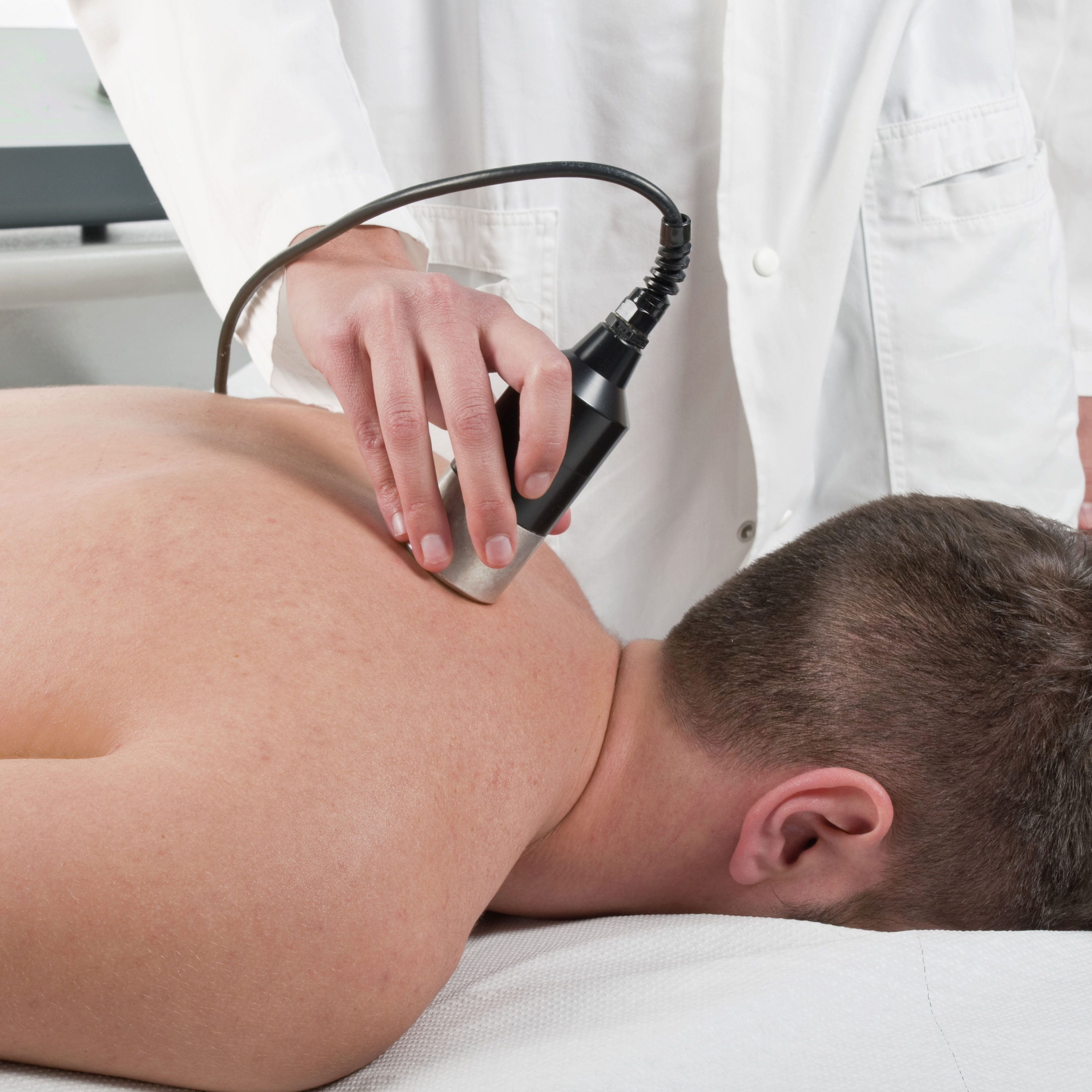 The image shows a person receiving a treatment on their back, with a therapist using a handheld device in a clinical setting.