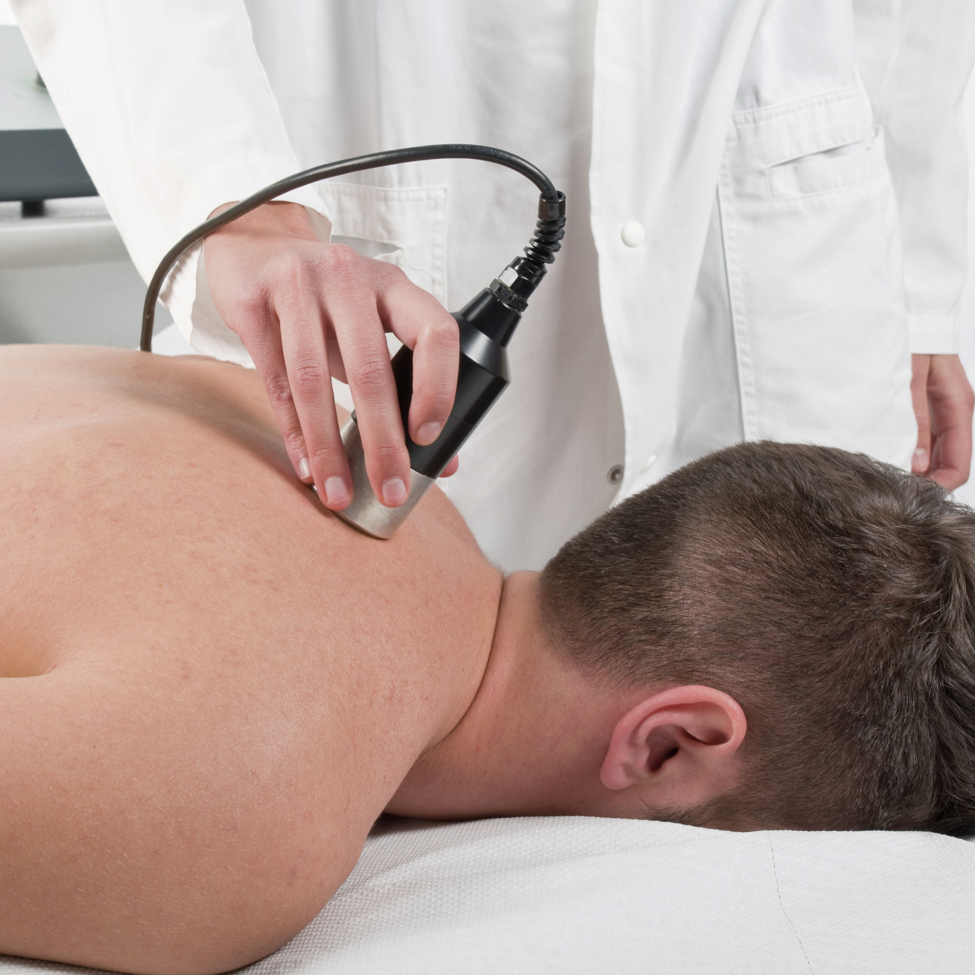 up close right side of white man face down getting laser treatment by female chiropractor doctor