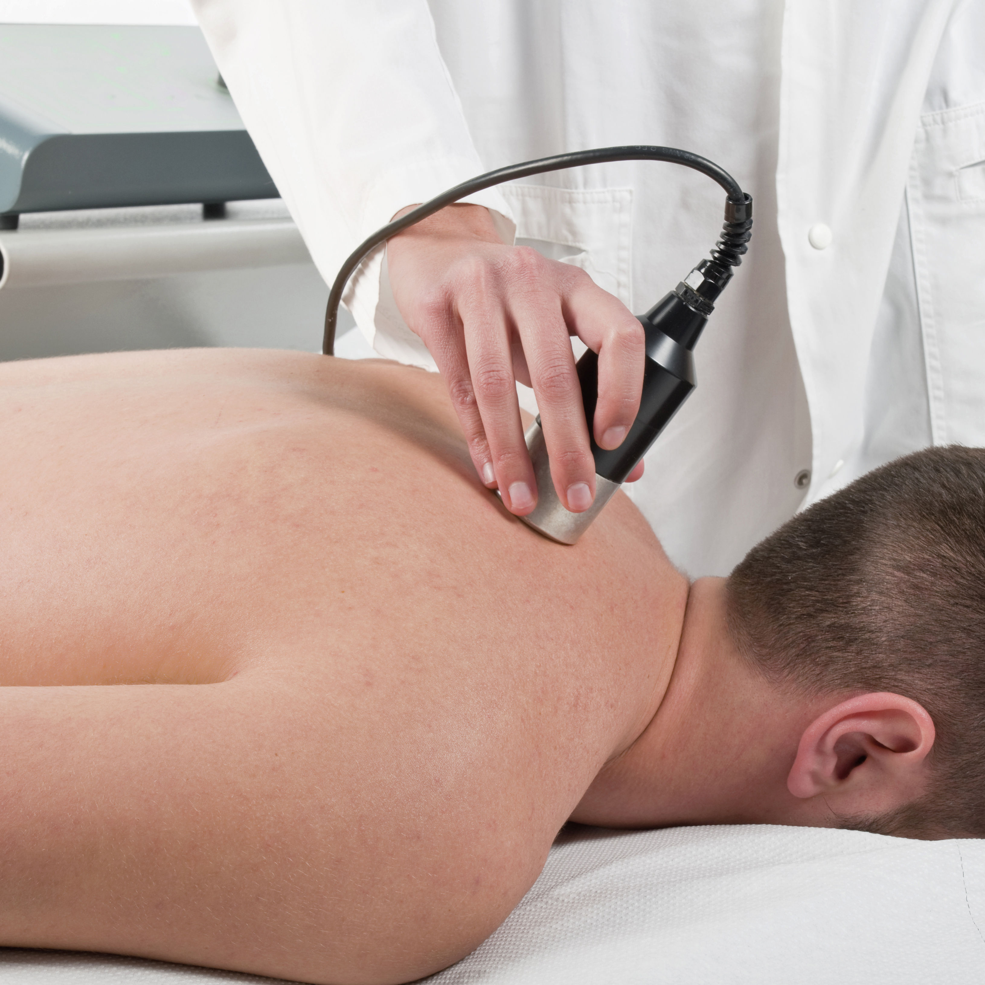 The image shows a person receiving a treatment on their back, with a therapist using a handheld device in a clinical setting.