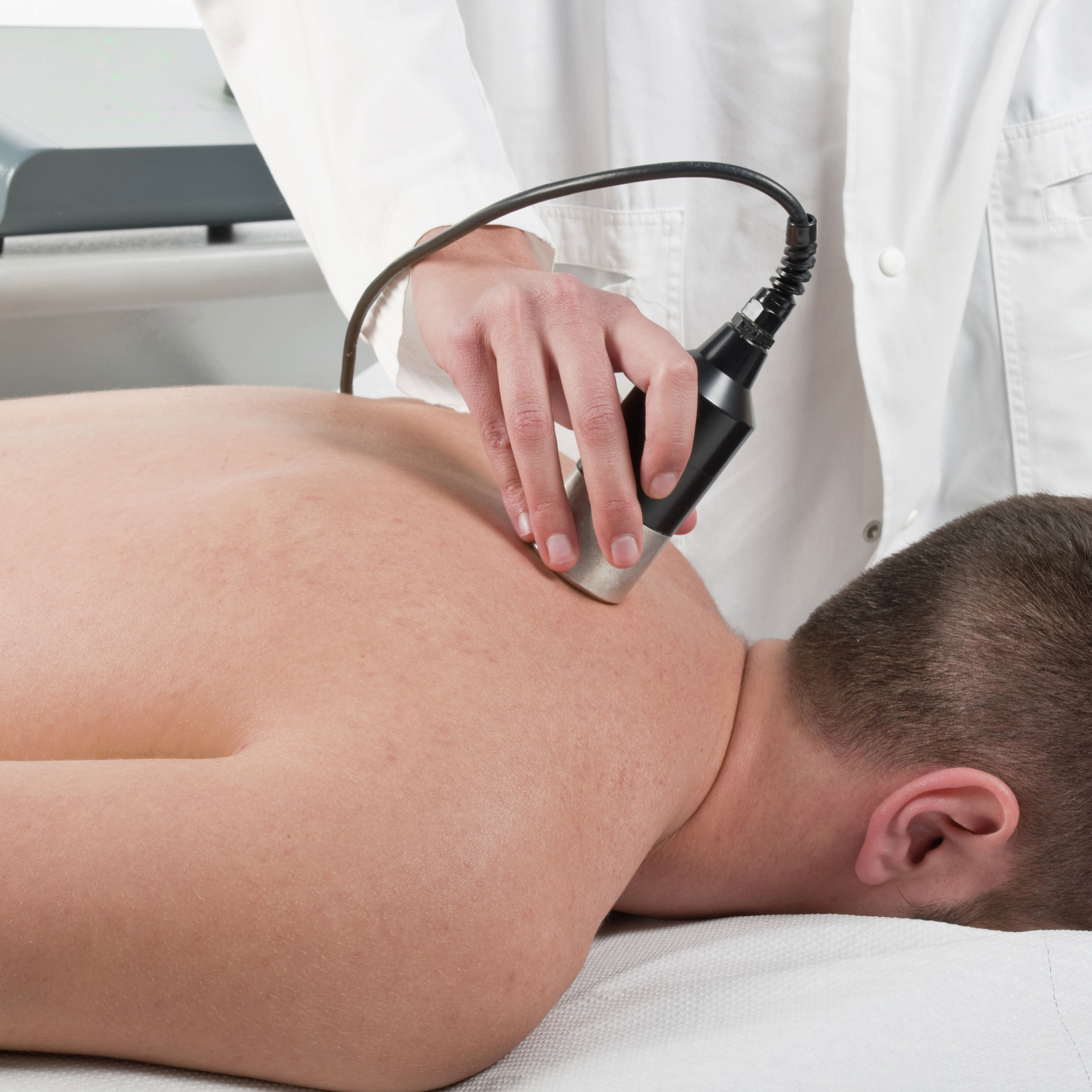 The image shows a person receiving a treatment on their back, with a therapist using a handheld device in a clinical setting.