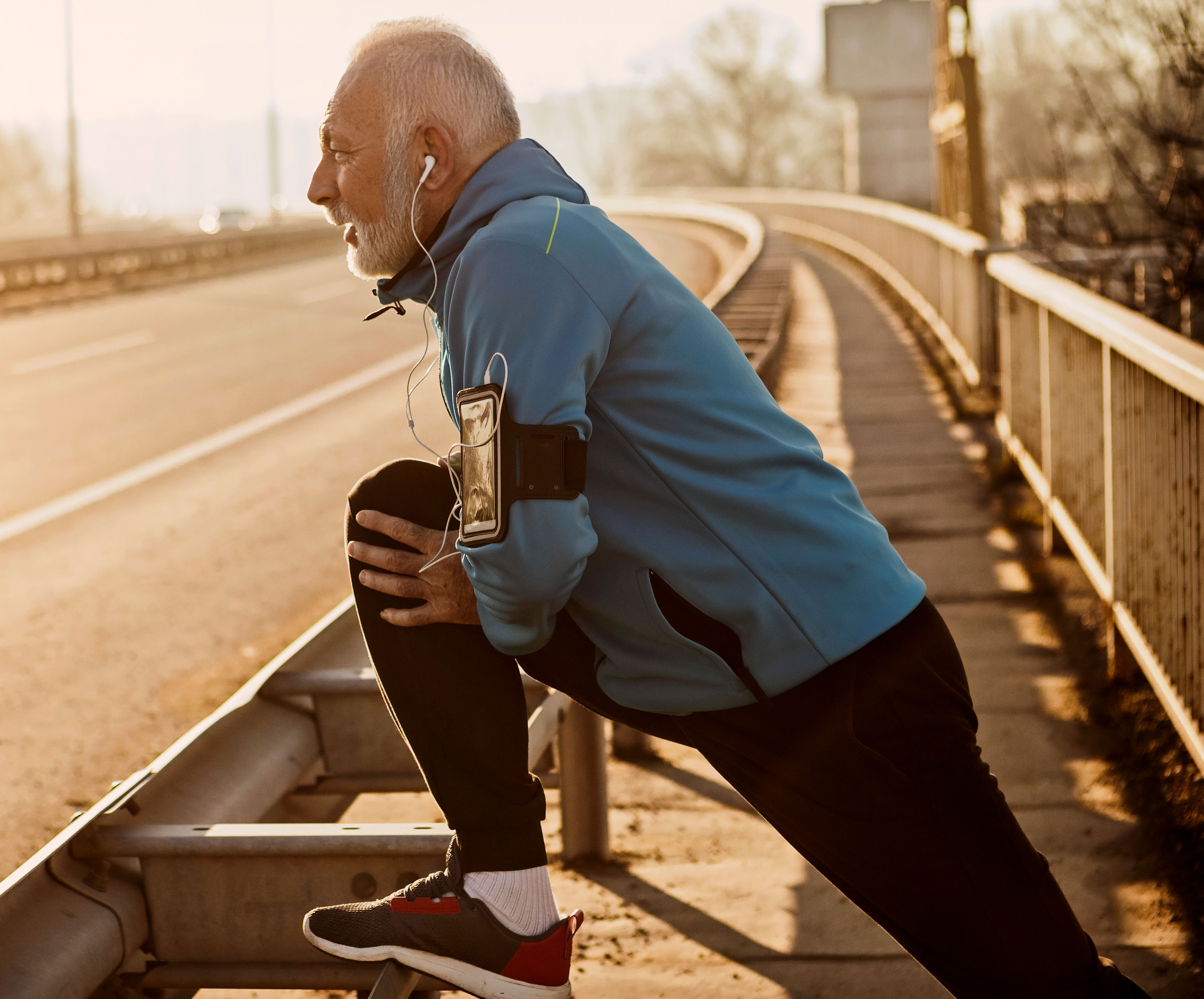 Senior man warming up for jogging on a city bridge