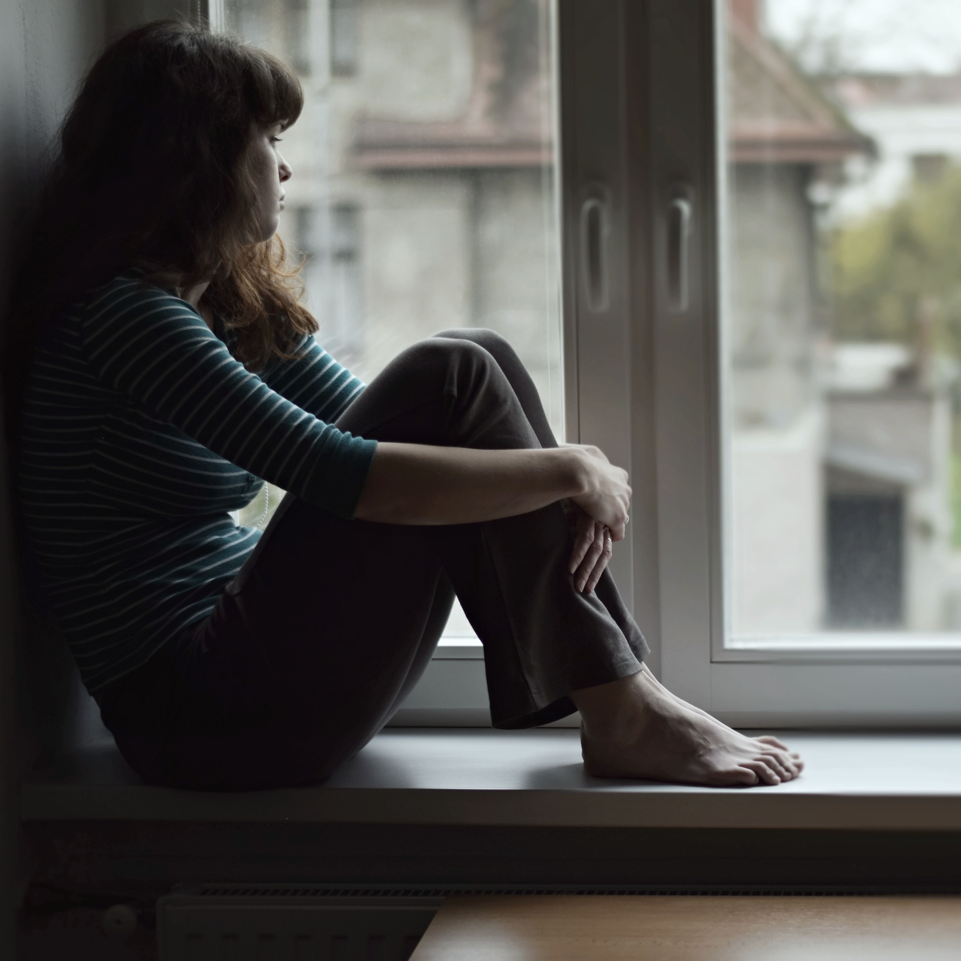 Sad young woman sitting on the window, watching ou