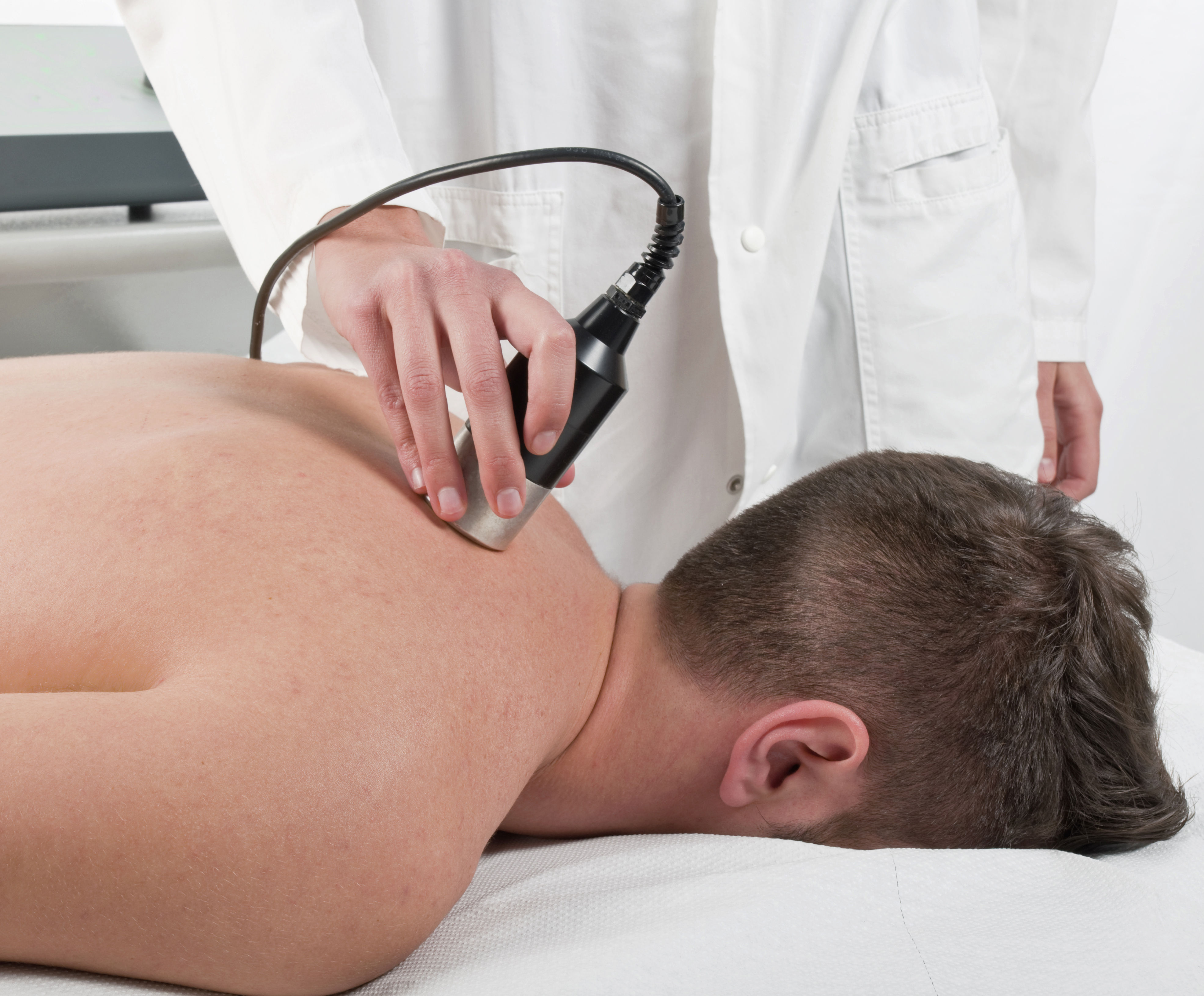 The image shows a person receiving a treatment on their back, with a therapist using a handheld device in a clinical setting.