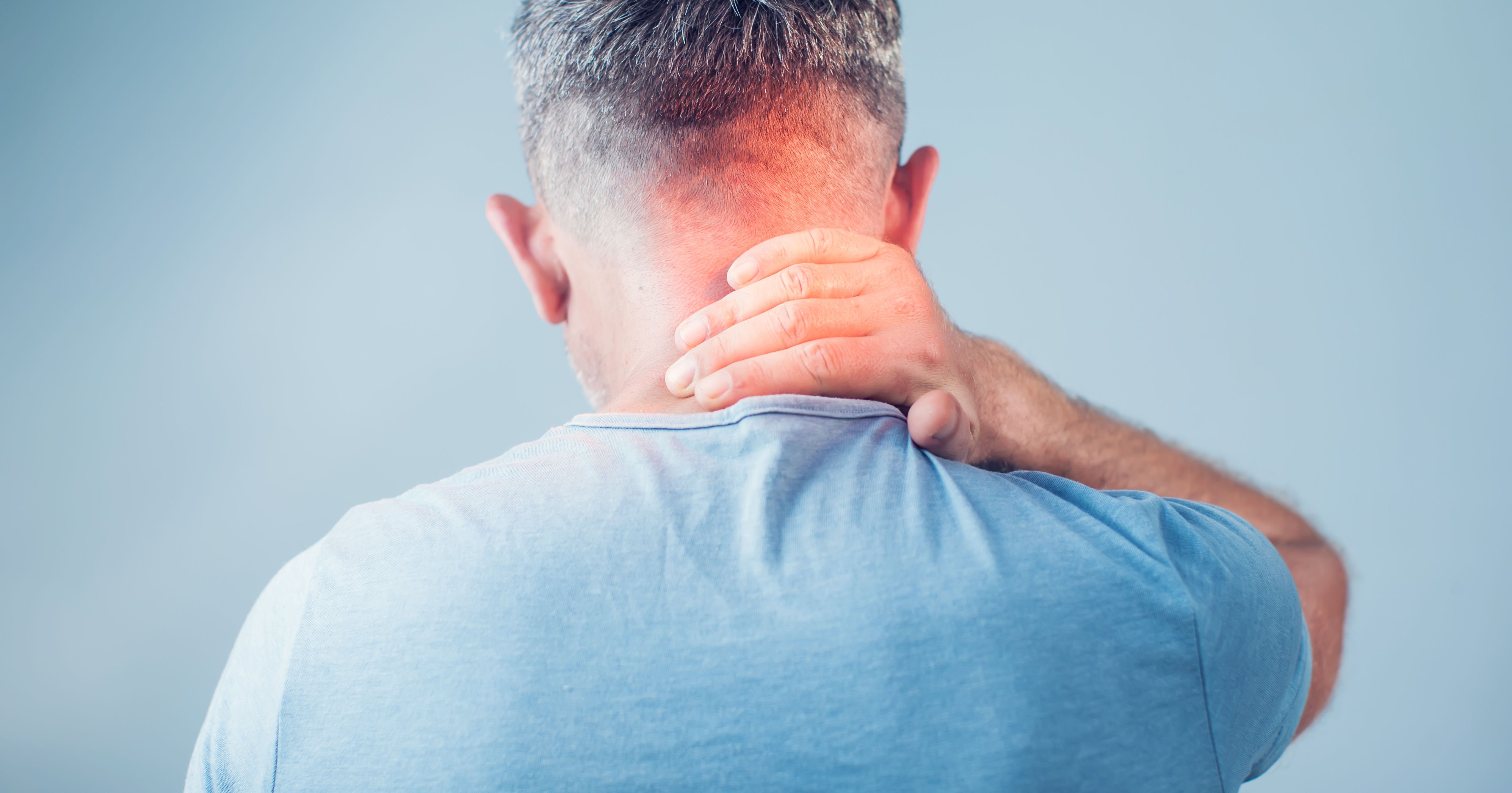 A person with short hair is touching the back of their neck, appearing to experience discomfort or tension. The background is a soft, blurred blue.