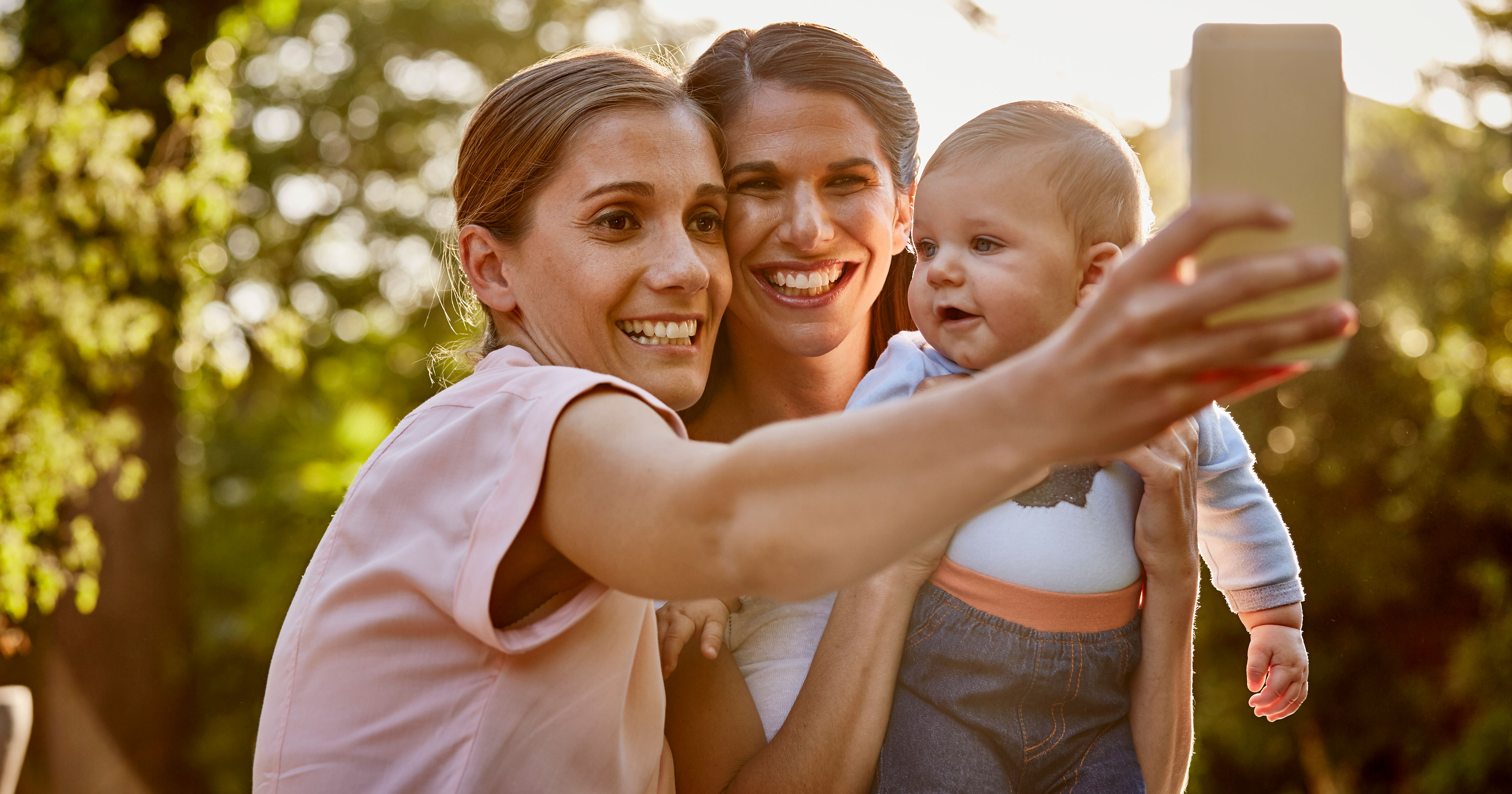 Lesbian couple with baby taking selfie in park