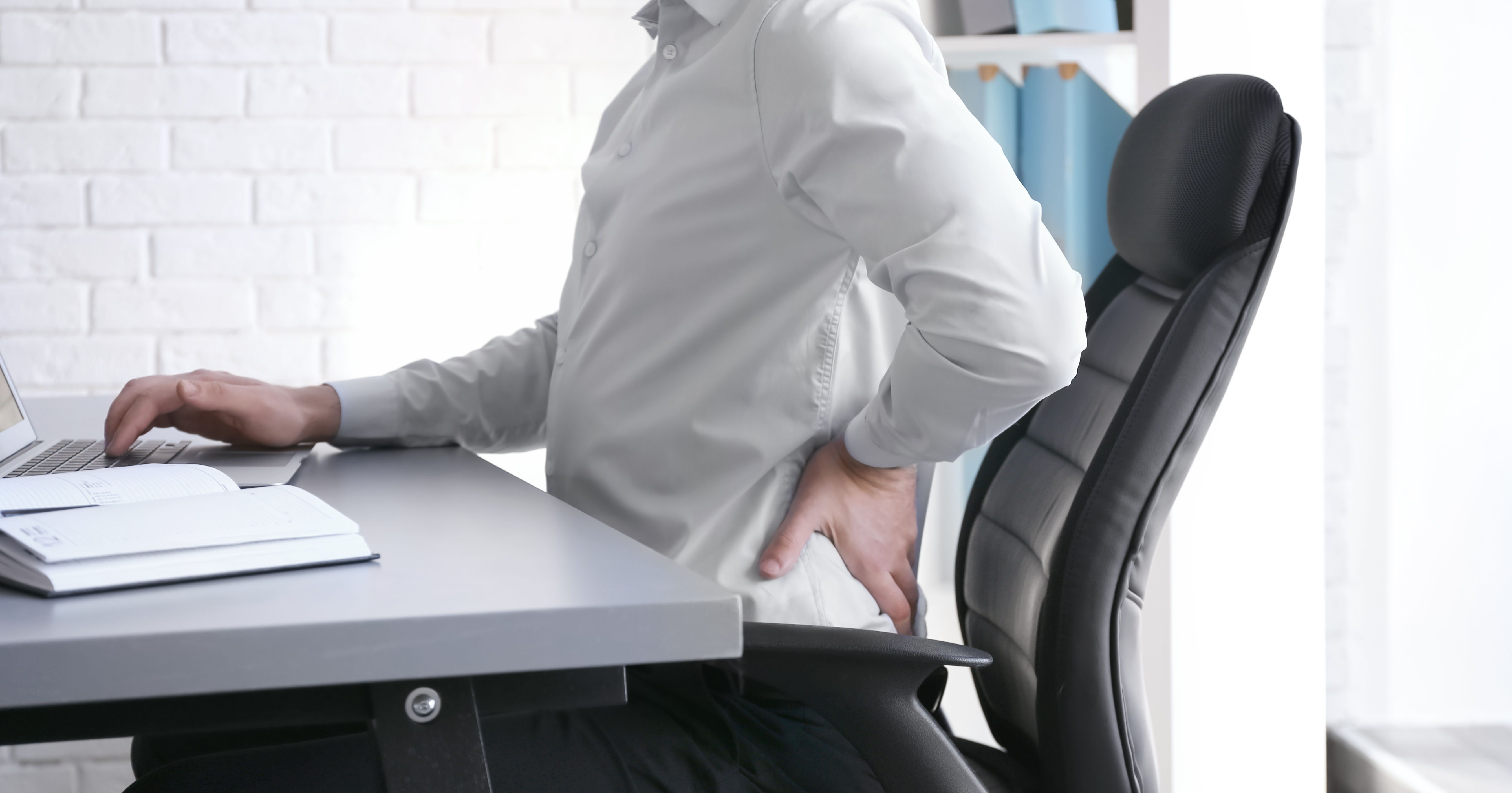 white male sitting at desk left side view with left arm holding low back pain
