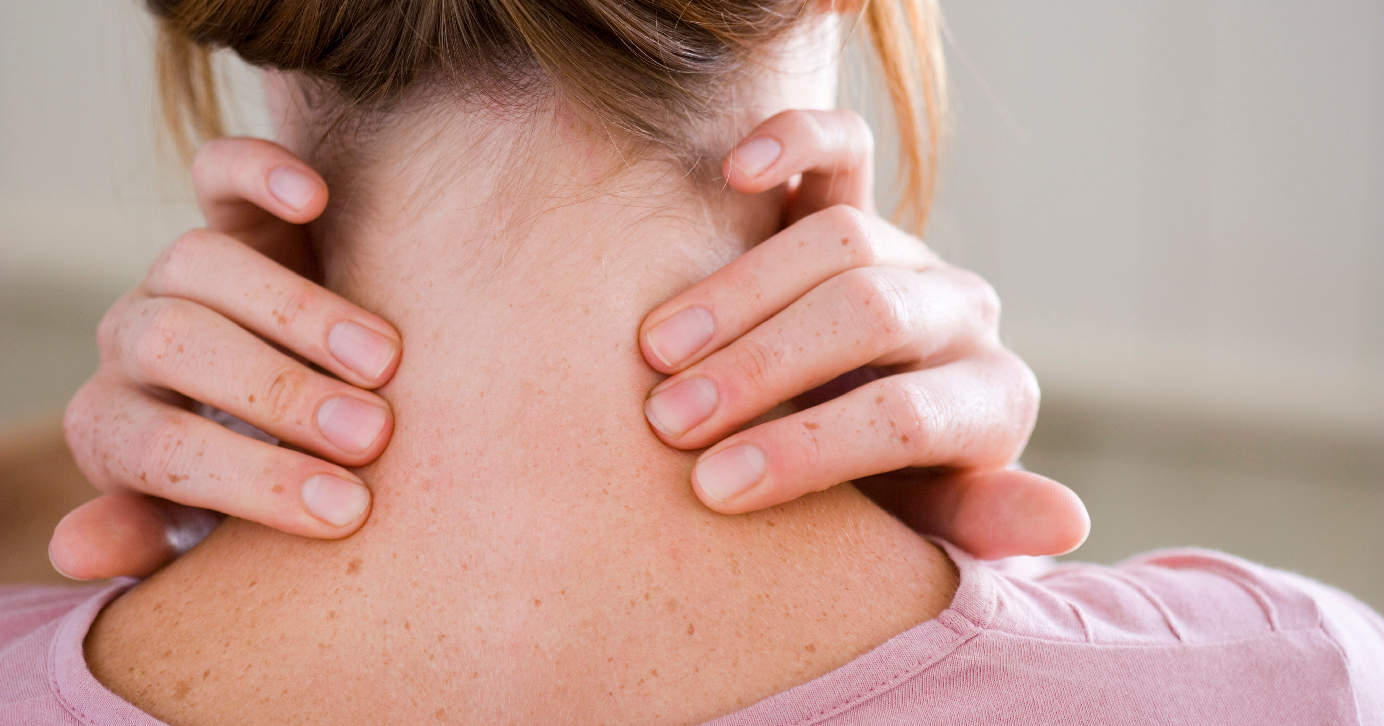 The image shows a close-up of a person's neck from the back, with their hands gripping the nape, suggesting tension or discomfort.